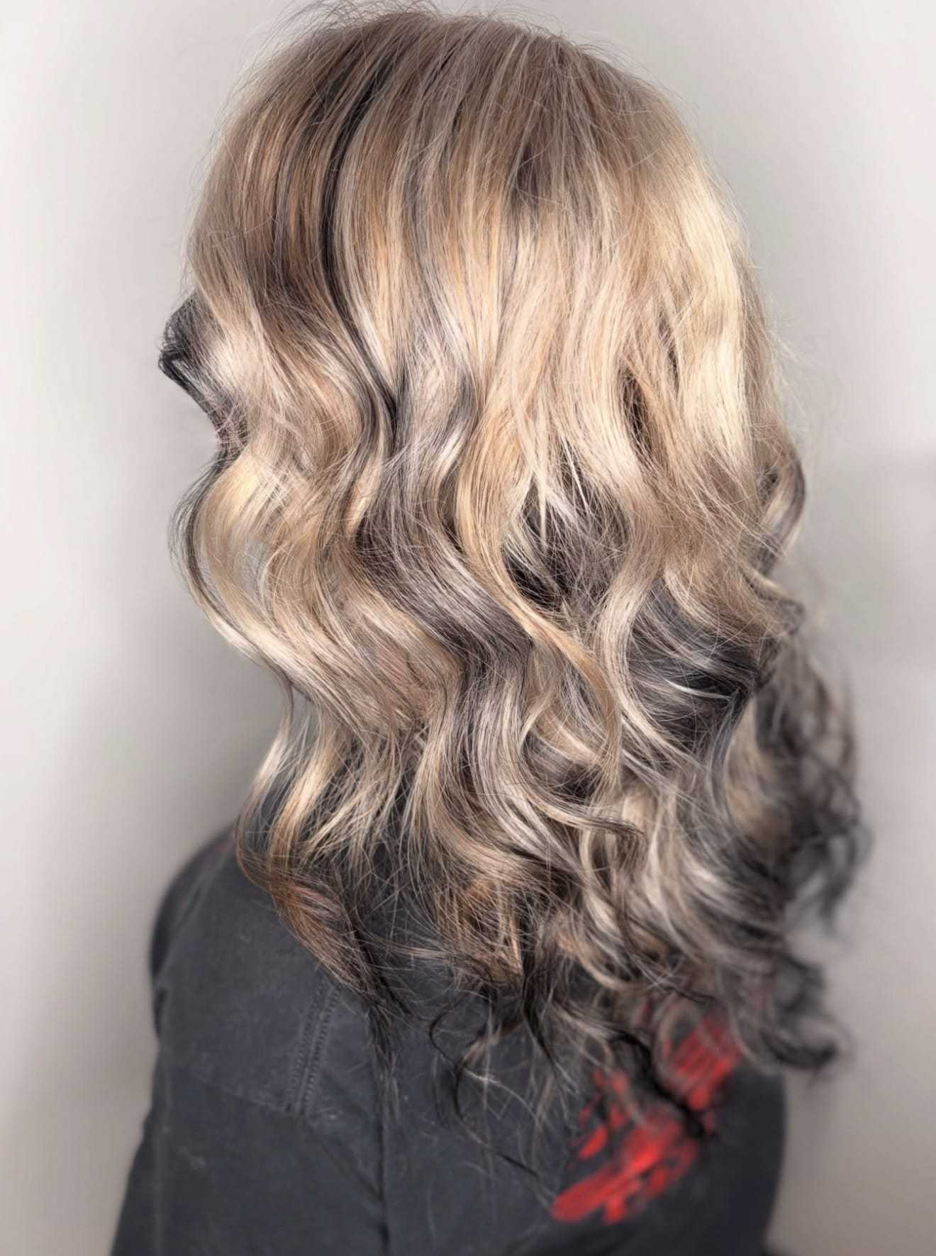 Wavy blonde hair with dark roots styled on a person wearing a dark top.