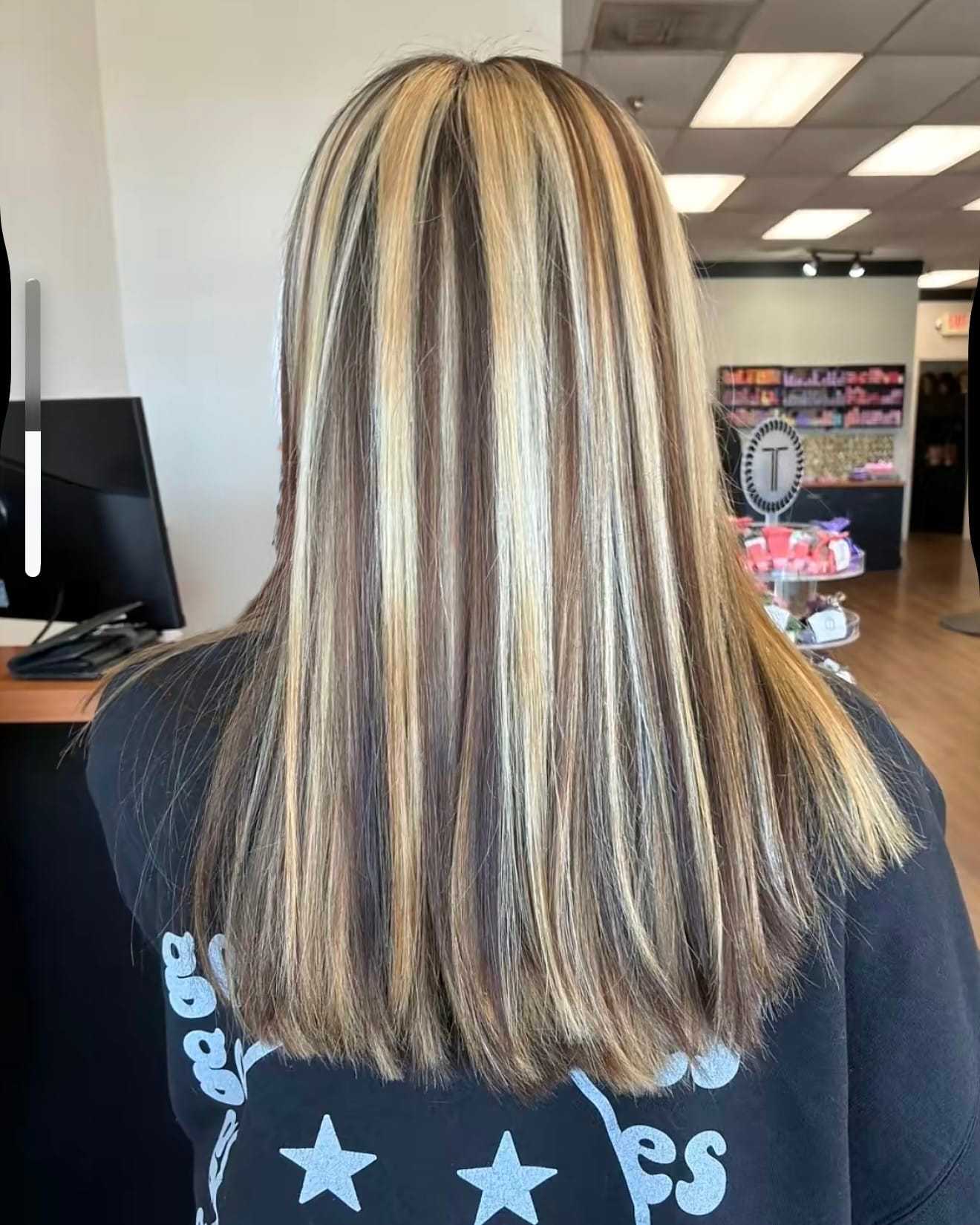 A person with long straight hair featuring blonde highlights, inside a salon.