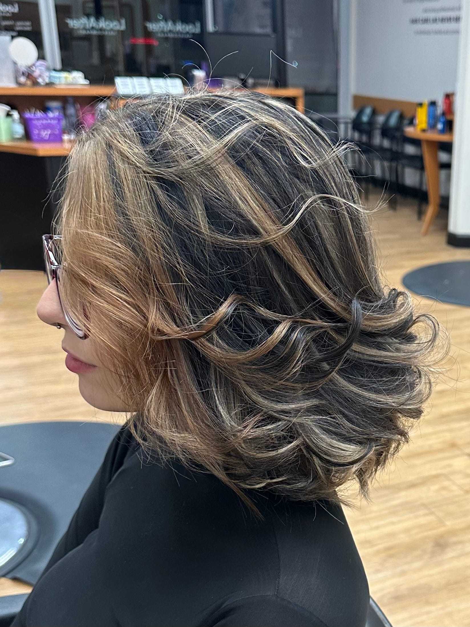 Woman with curly, shoulder-length hair and glasses in a salon setting.