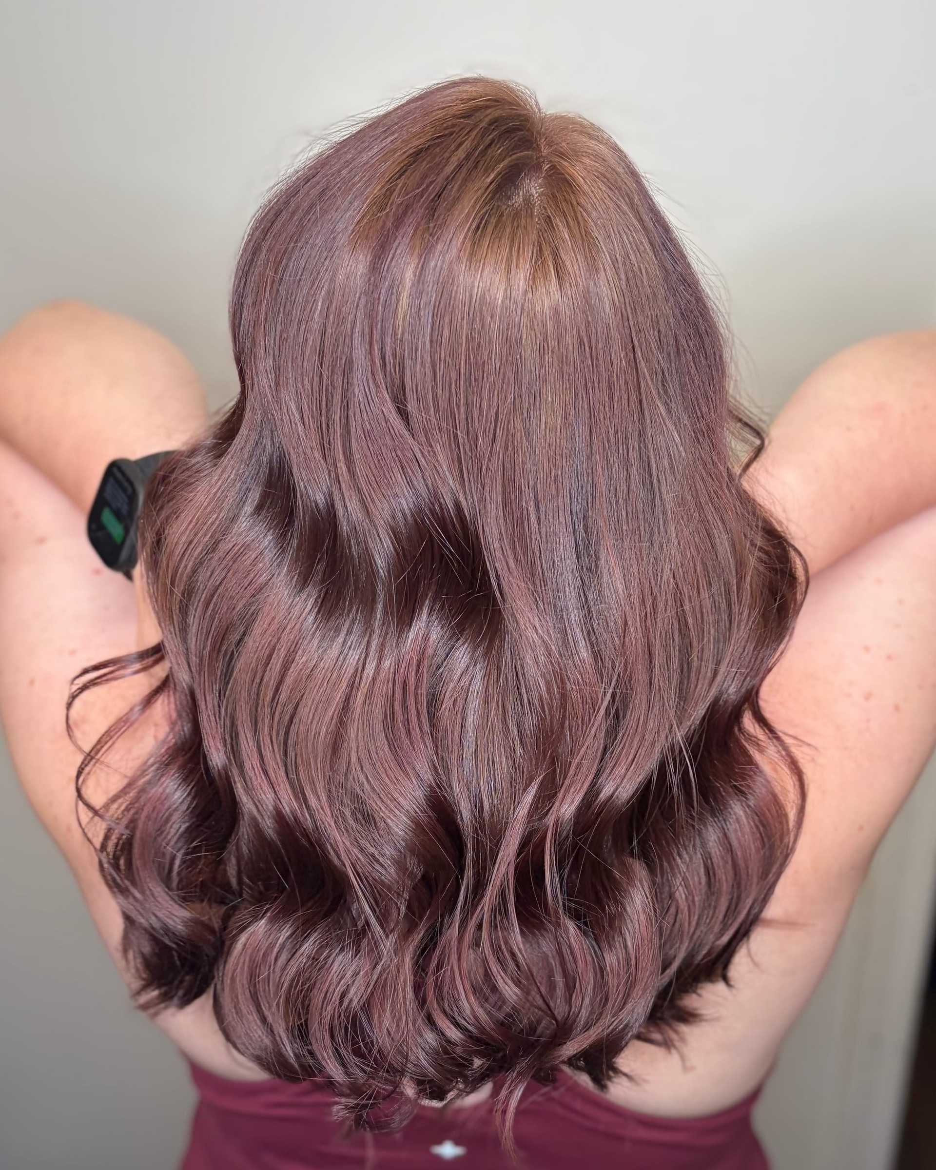 A person showing wavy, brownish-purple hair from the back with arms raised.