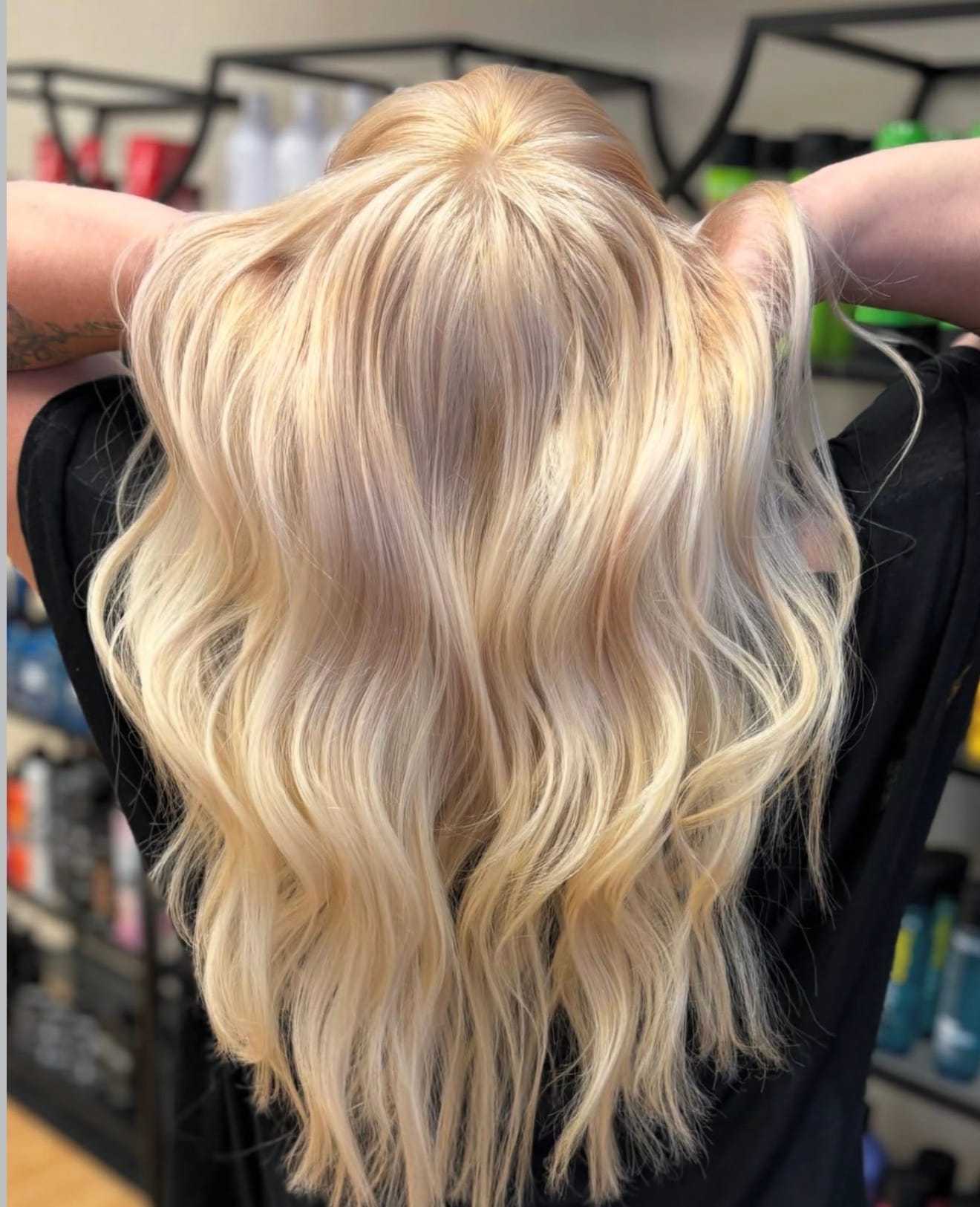 Blonde wavy hair styled in a salon, surrounded by shelves of hair products.