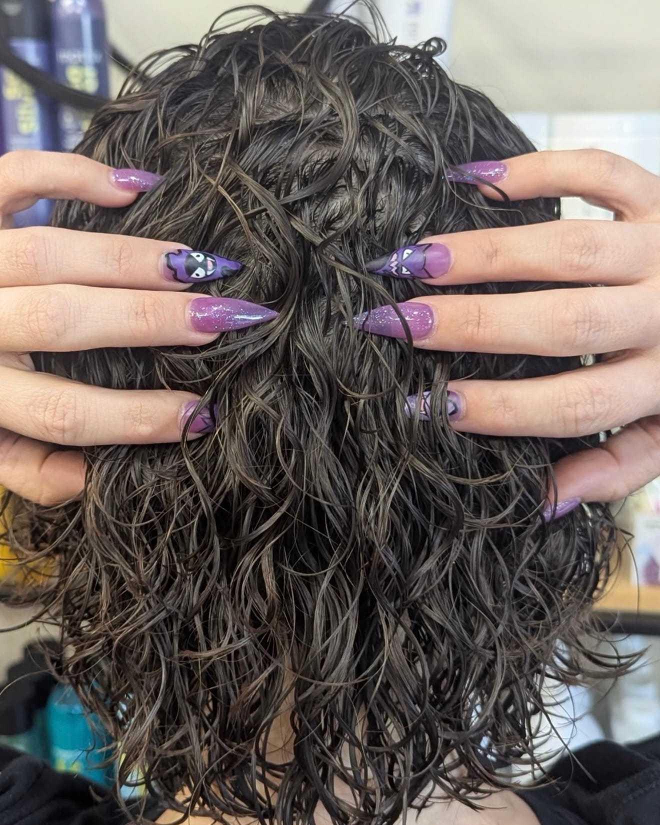 Person with purple-painted nails shows off curly, wet hair from the back.