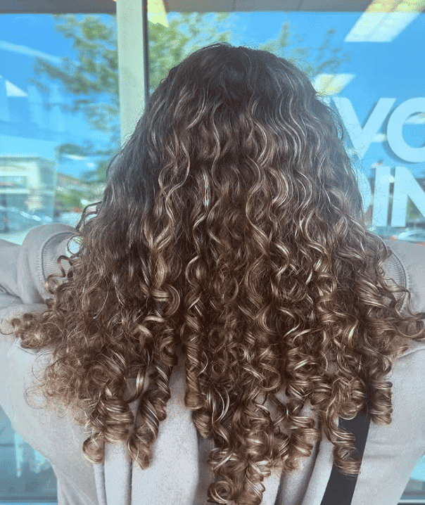 Curly-haired person standing in front of a window, facing away.