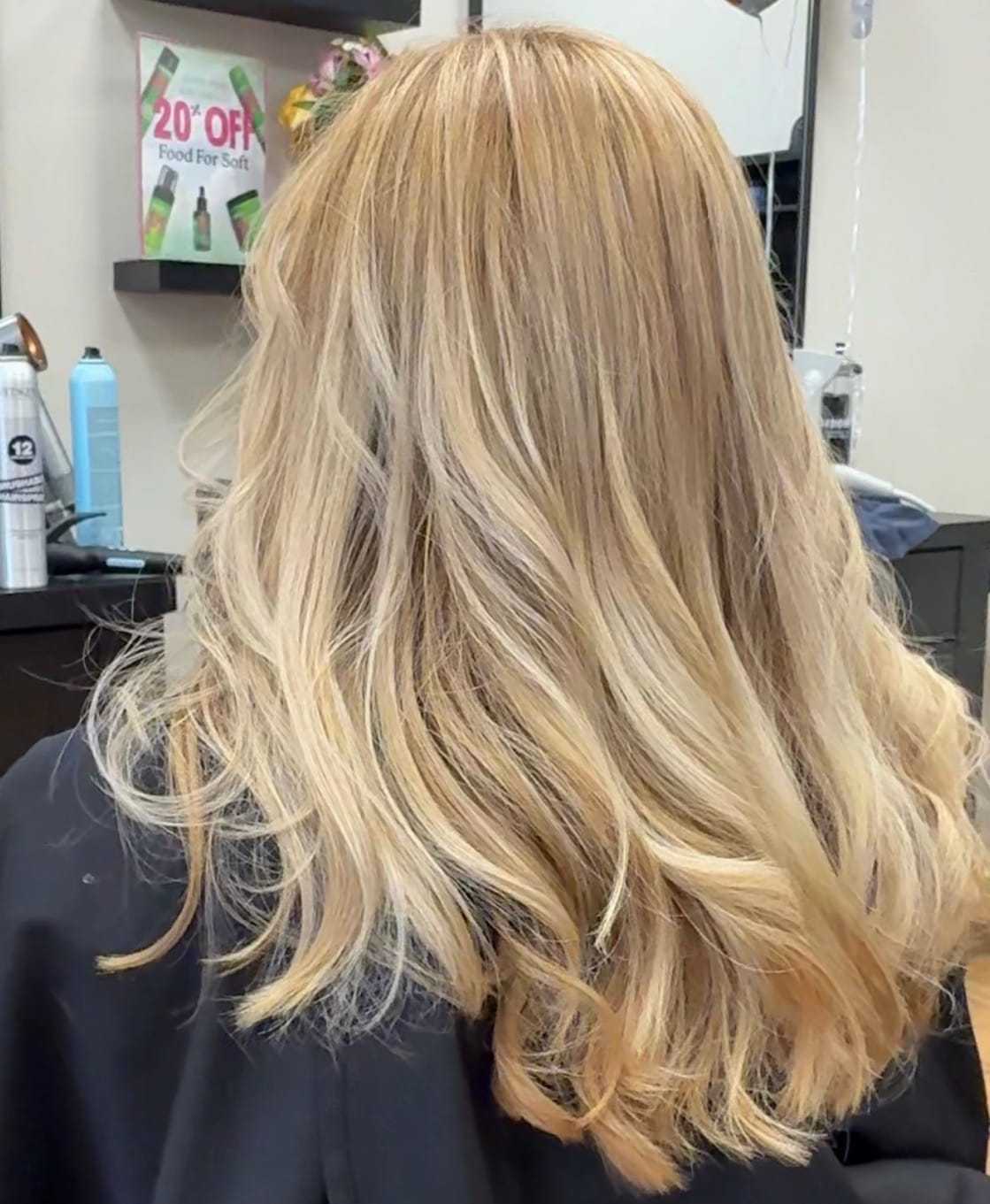Blonde hair styled in soft waves at a salon, with hair care products in the background.