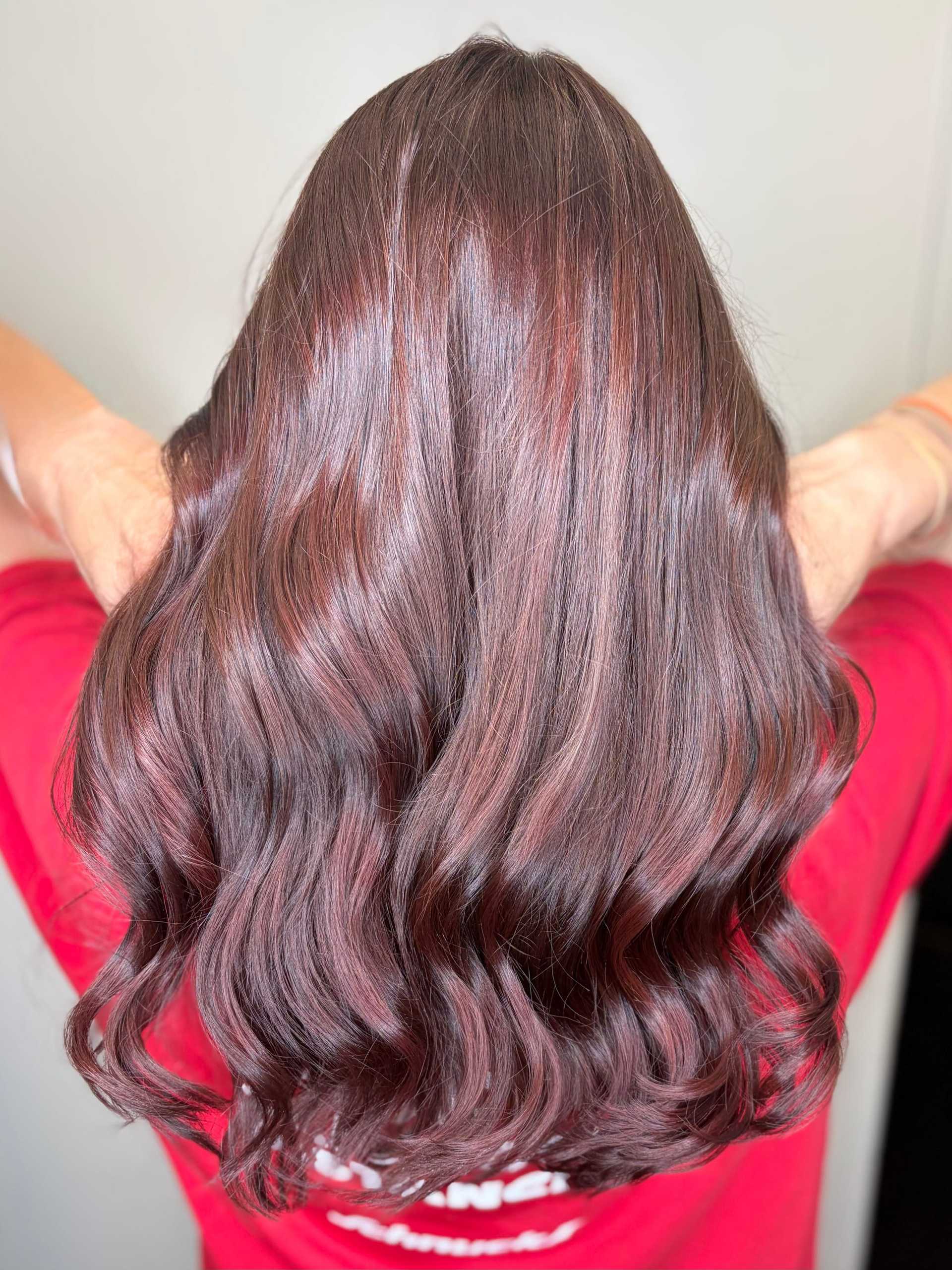 A person with wavy, dark brown hair in a vibrant red shirt seen from the back.
