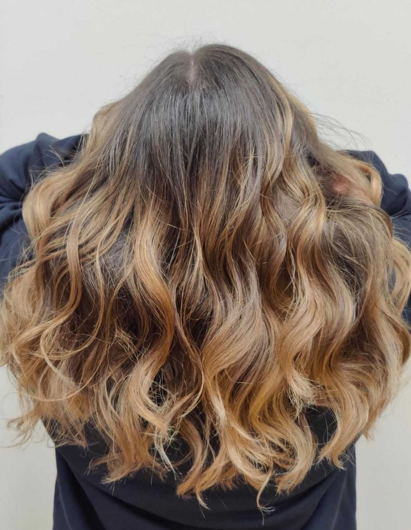 Wavy hair with brown highlights cascading down the back against a plain backdrop.