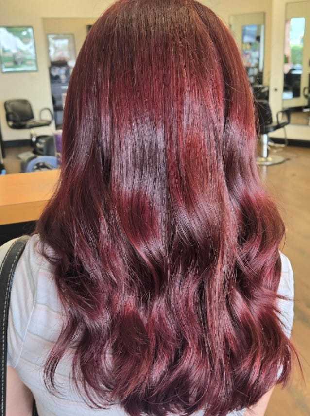 Back view of a person with wavy, rich burgundy hair in a salon setting.
