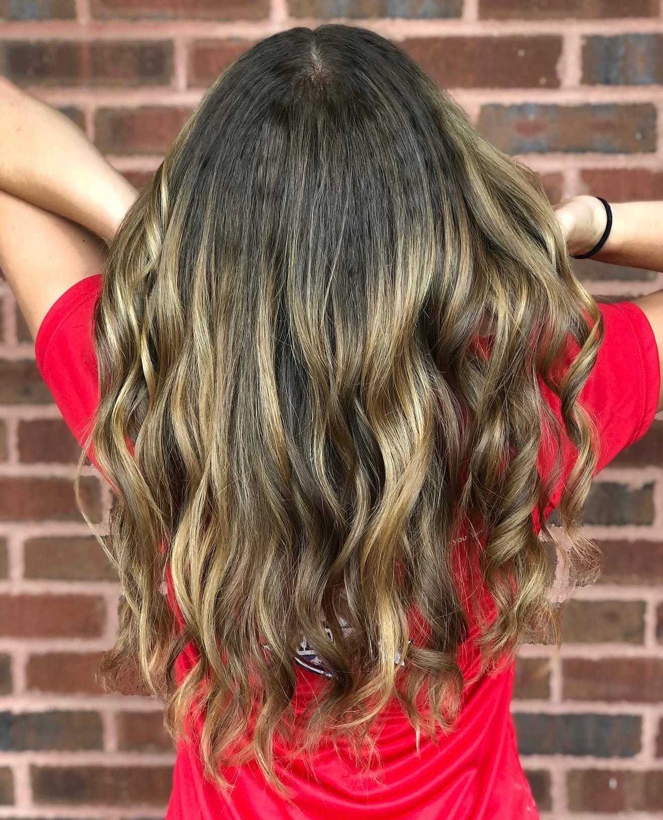 Wavy, highlighted hair flowing down the back of a person in a red shirt, against a brick wall.