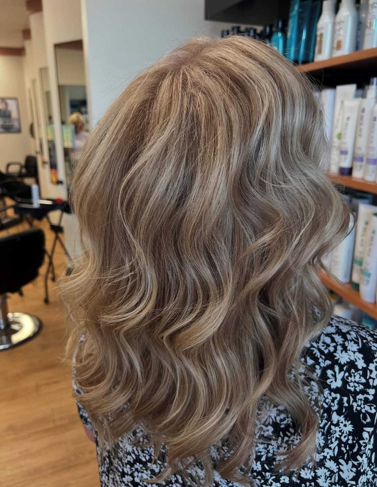 Wavy blonde hairstyle in a salon setting with hair products on shelves.