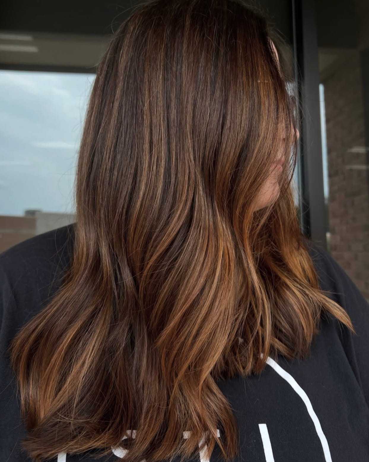 Woman with long, wavy brown hair and subtle highlights, standing in front of a window.