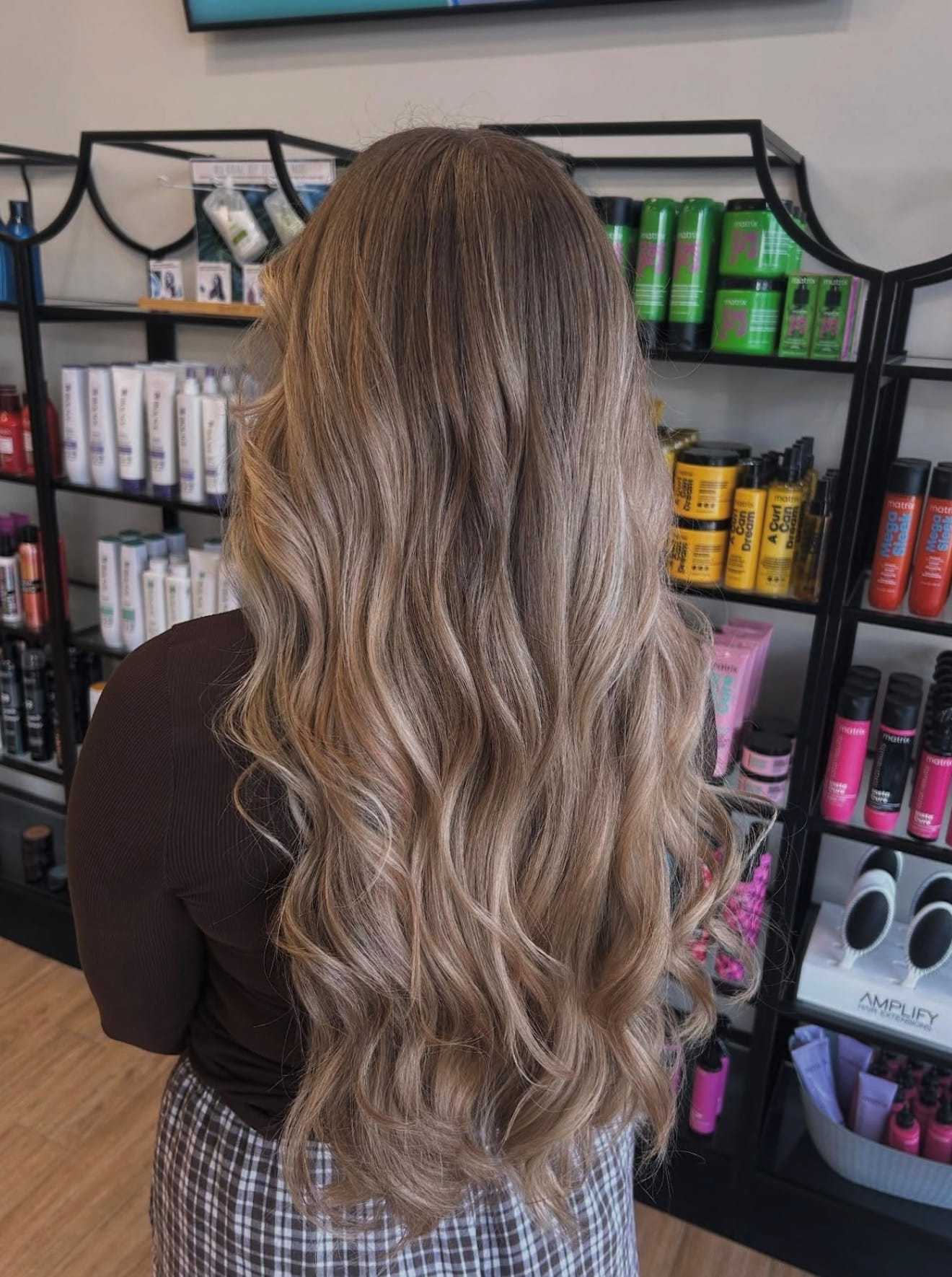 Long wavy blonde hair in a salon, with hair products displayed on shelves.