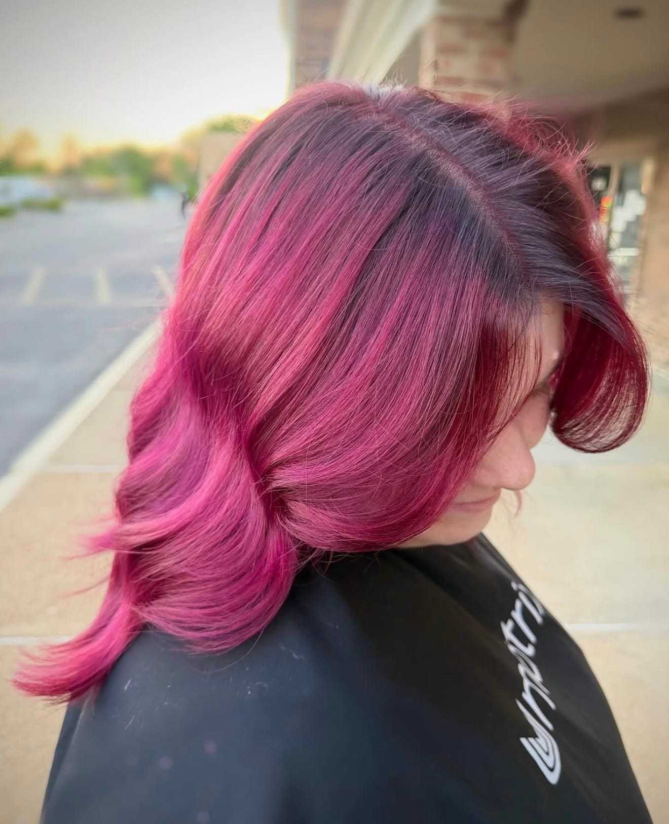 Pink ombre hair styled in waves, side view in an outdoor setting.