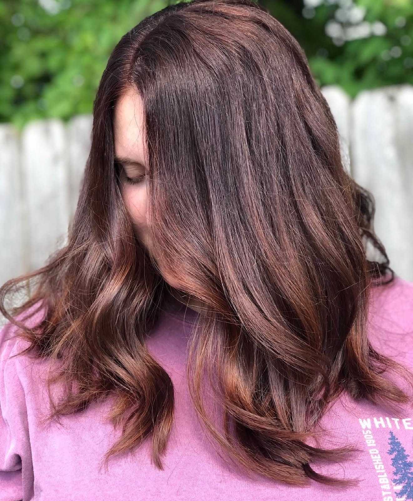 Woman with long, wavy, chestnut-brown hair wearing a pink shirt.