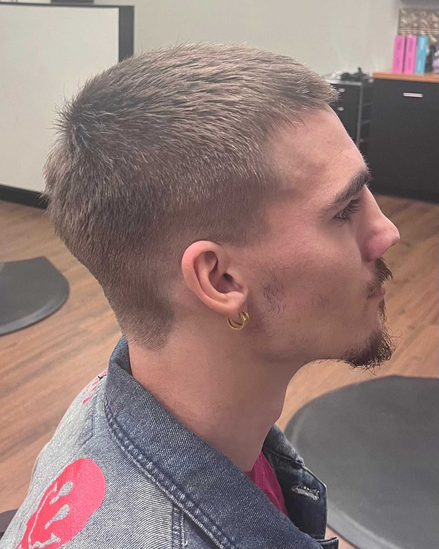 Man with short haircut and earrings, wearing a denim jacket in a salon setting.
