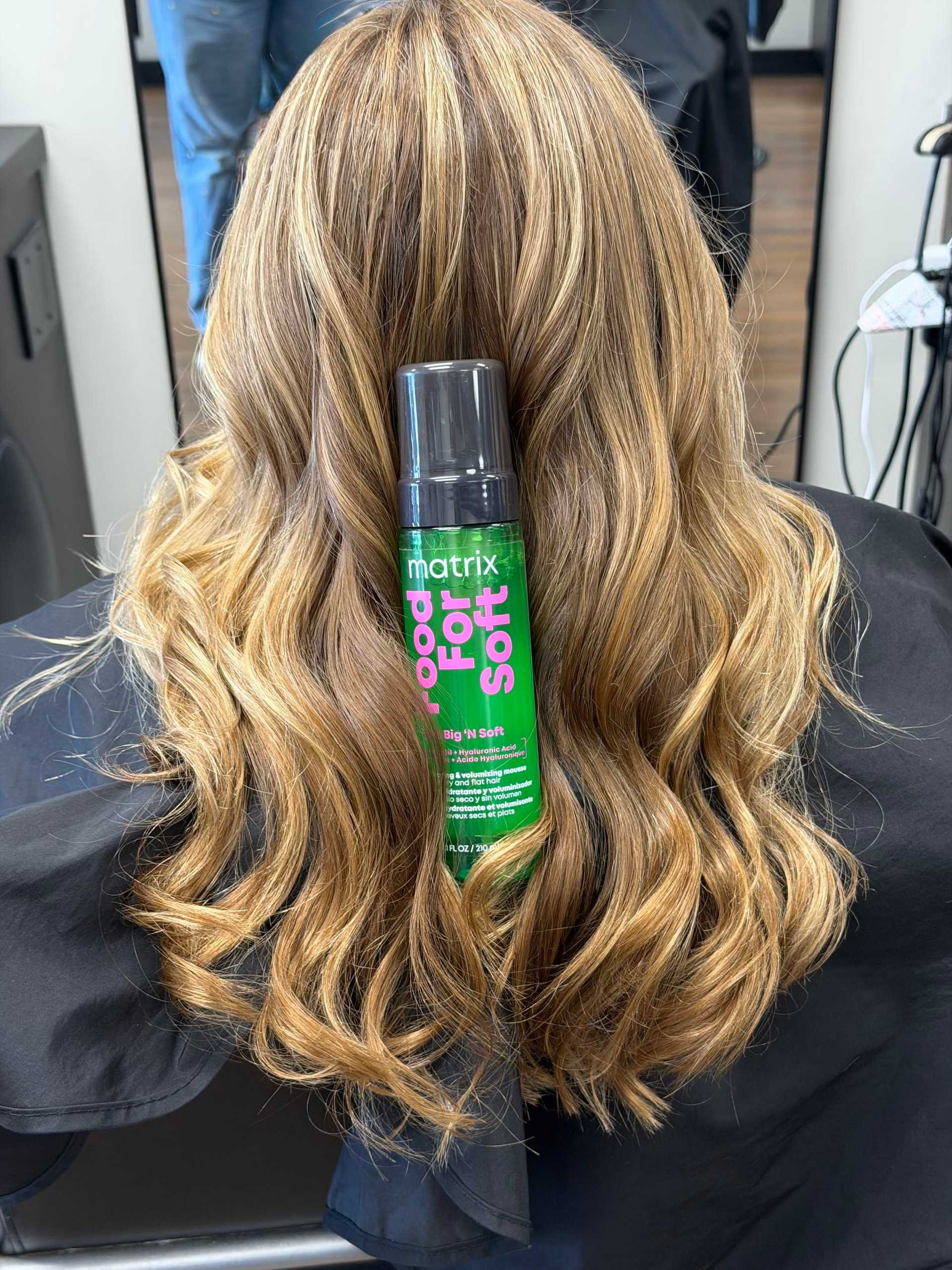 Blonde hair styled with curls, showcasing a bottle of Matrix styling foam for soft texture.