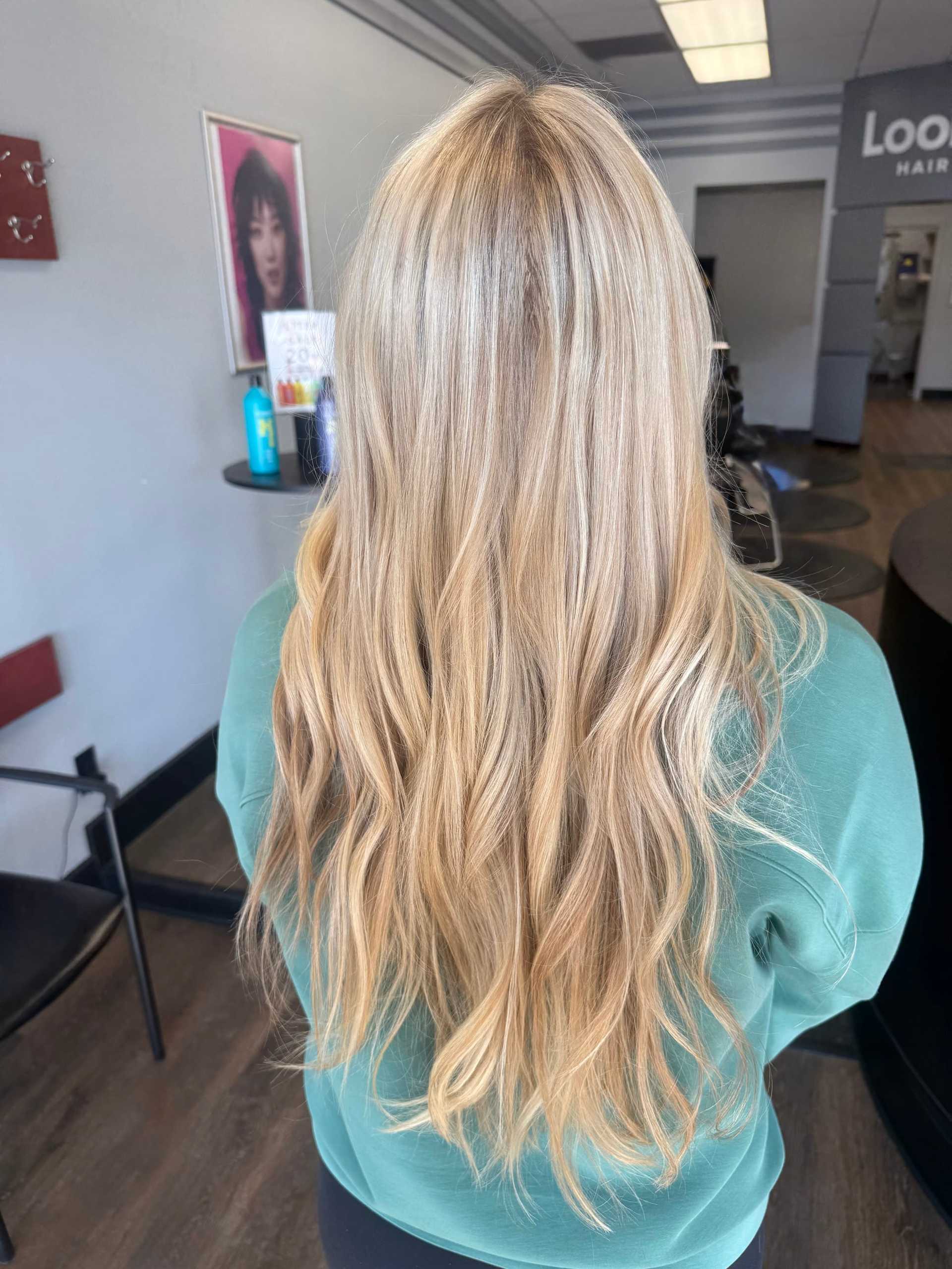 Long blonde hair with soft waves, styled in a salon, wearing a green top.
