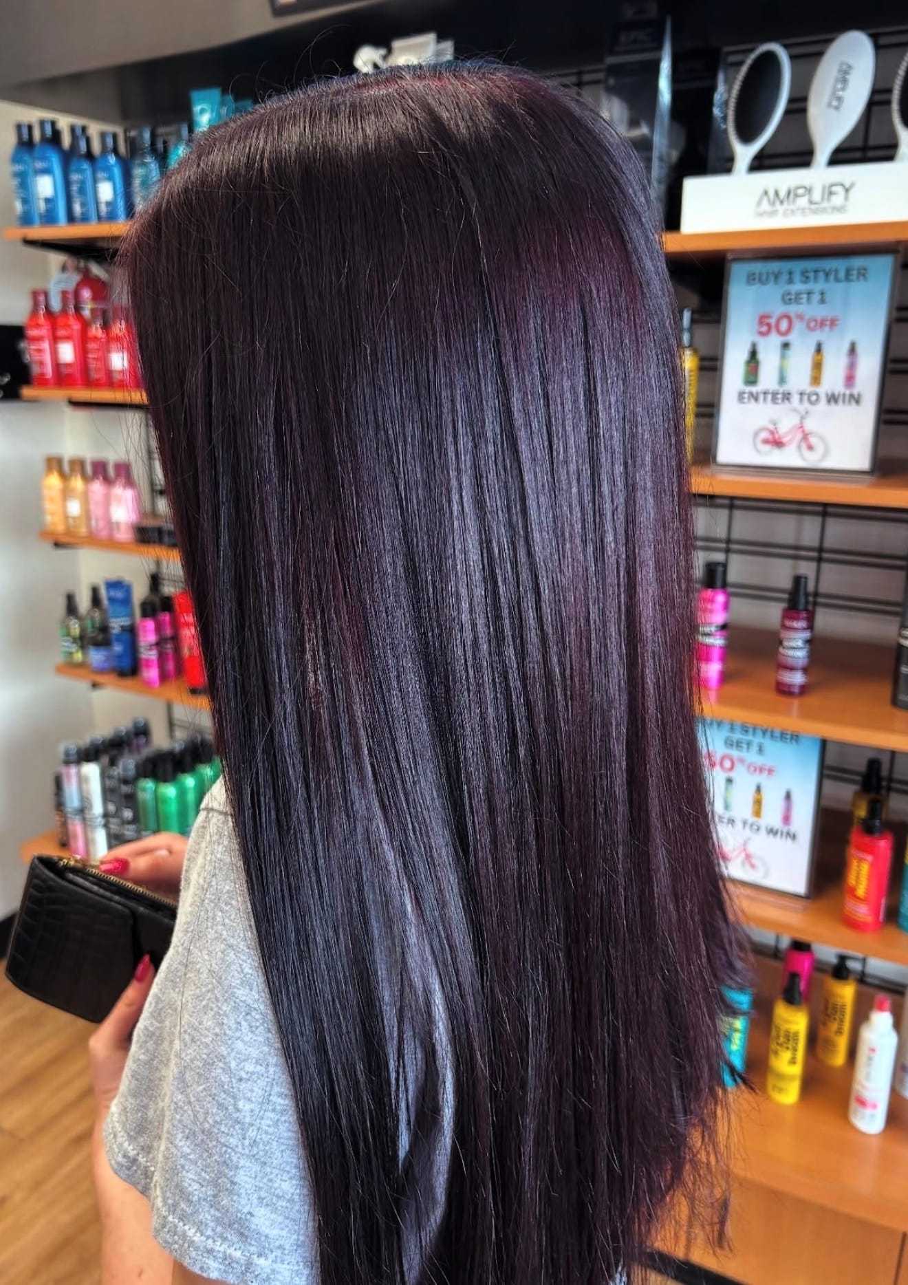 Woman with long, straight dark hair in a salon, surrounded by hair products.