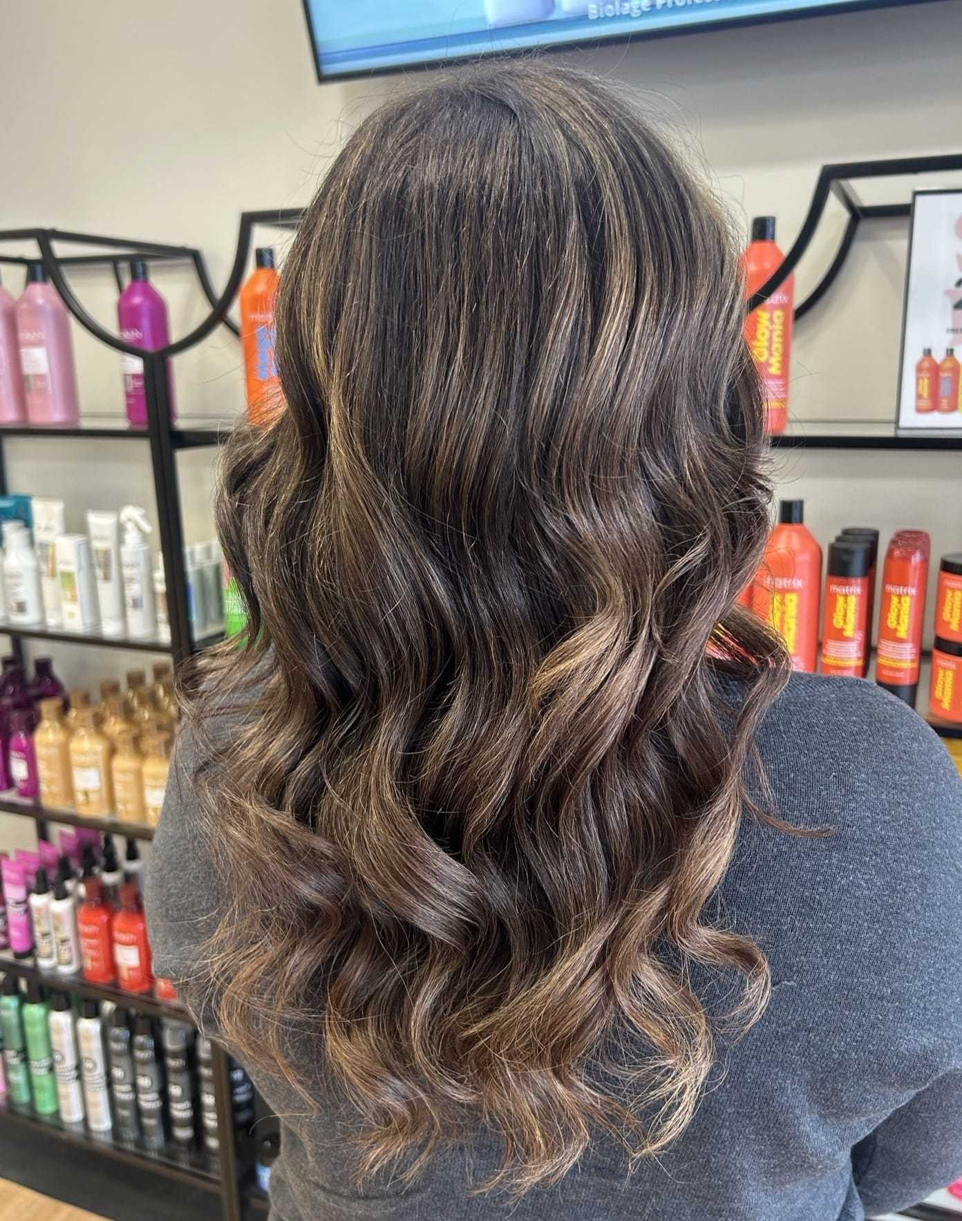 Wavy, brunette hairstyle in a salon setting with colorful hair products on display.
