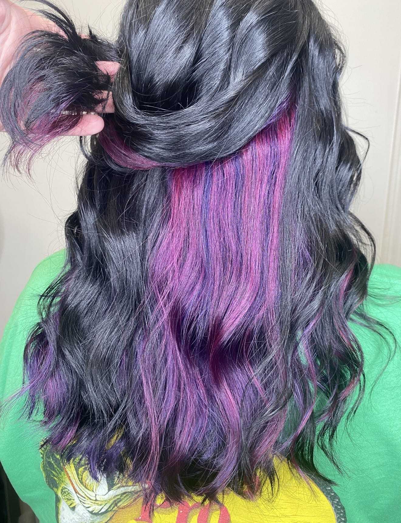 Black hair with pink highlights being styled, shown from the back, on a person in a green shirt.
