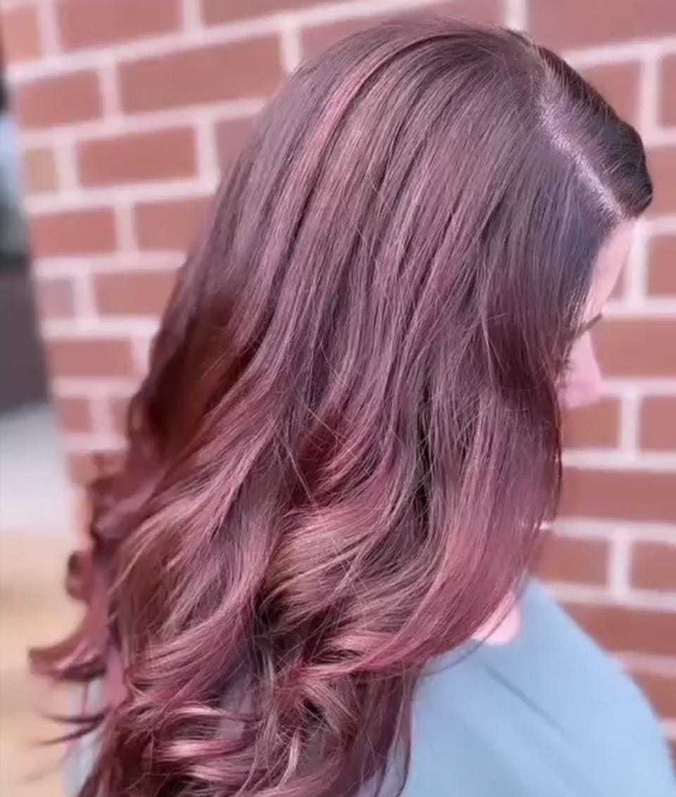 Woman with long, wavy, dyed pink hair against a brick wall background.