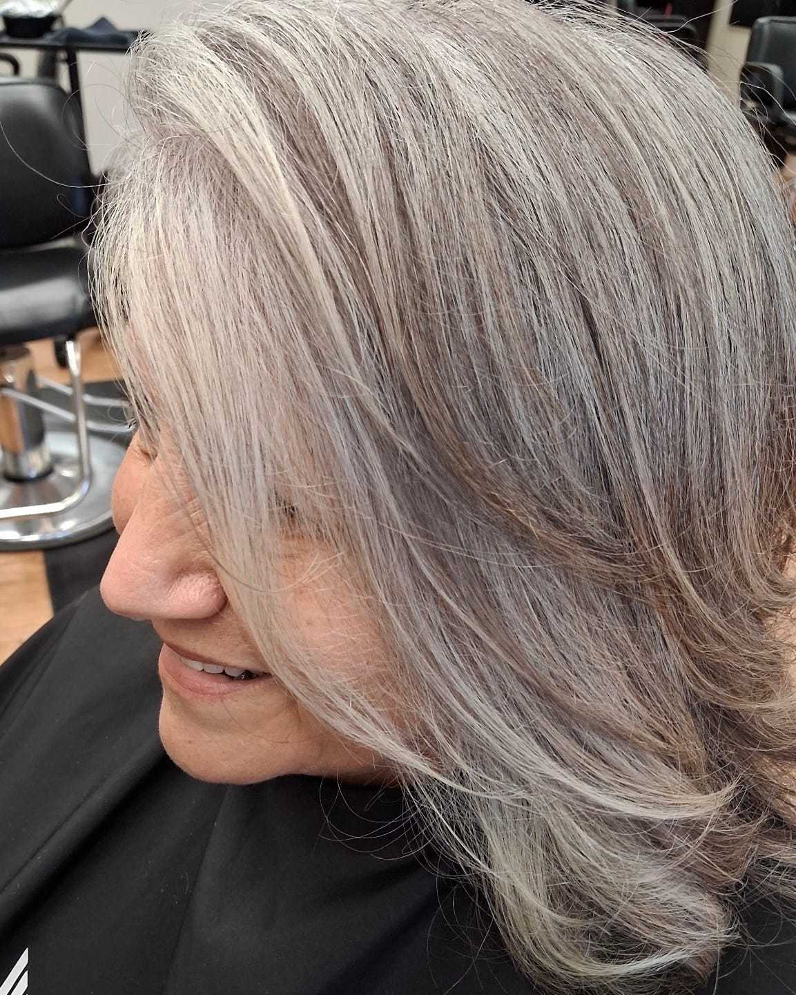 Woman with gray hair getting a haircut in a salon, smiling while seated.