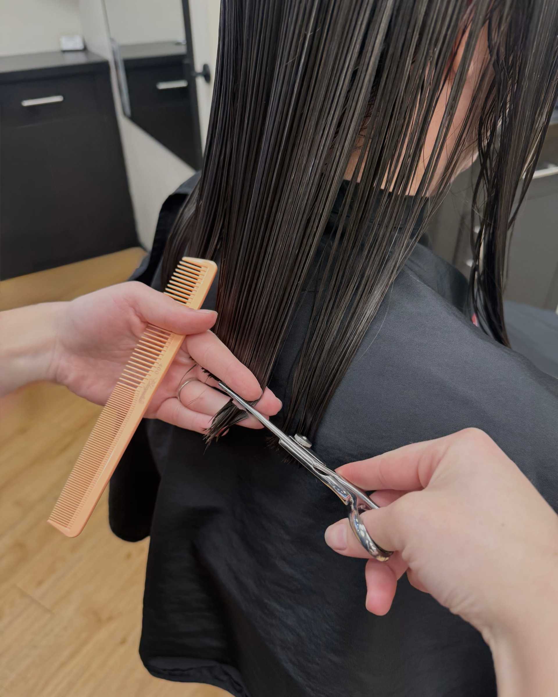 Haircut in progress with stylist trimming wet hair using scissors and comb.