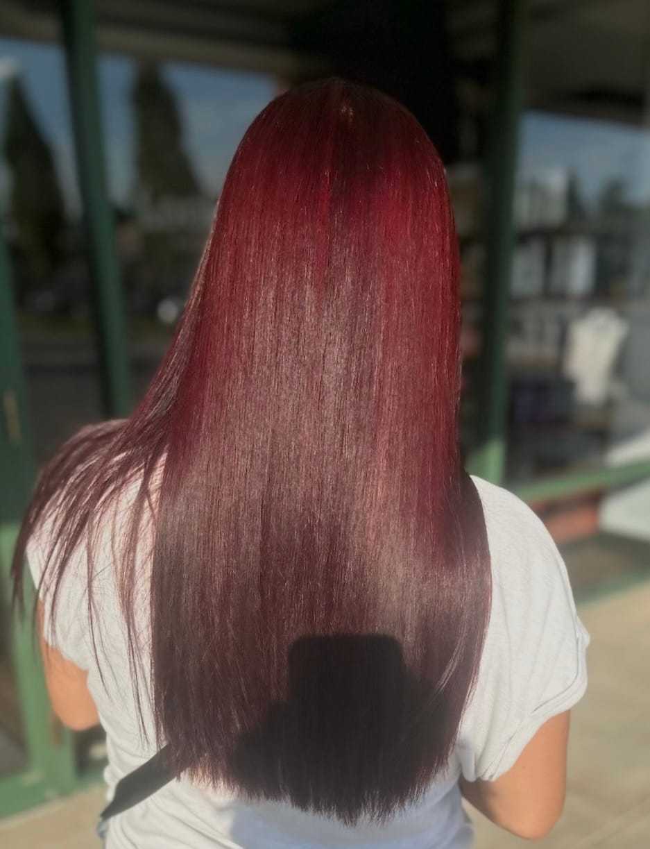 Long, straight burgundy hair in sunlight, seen from behind, outside a salon.