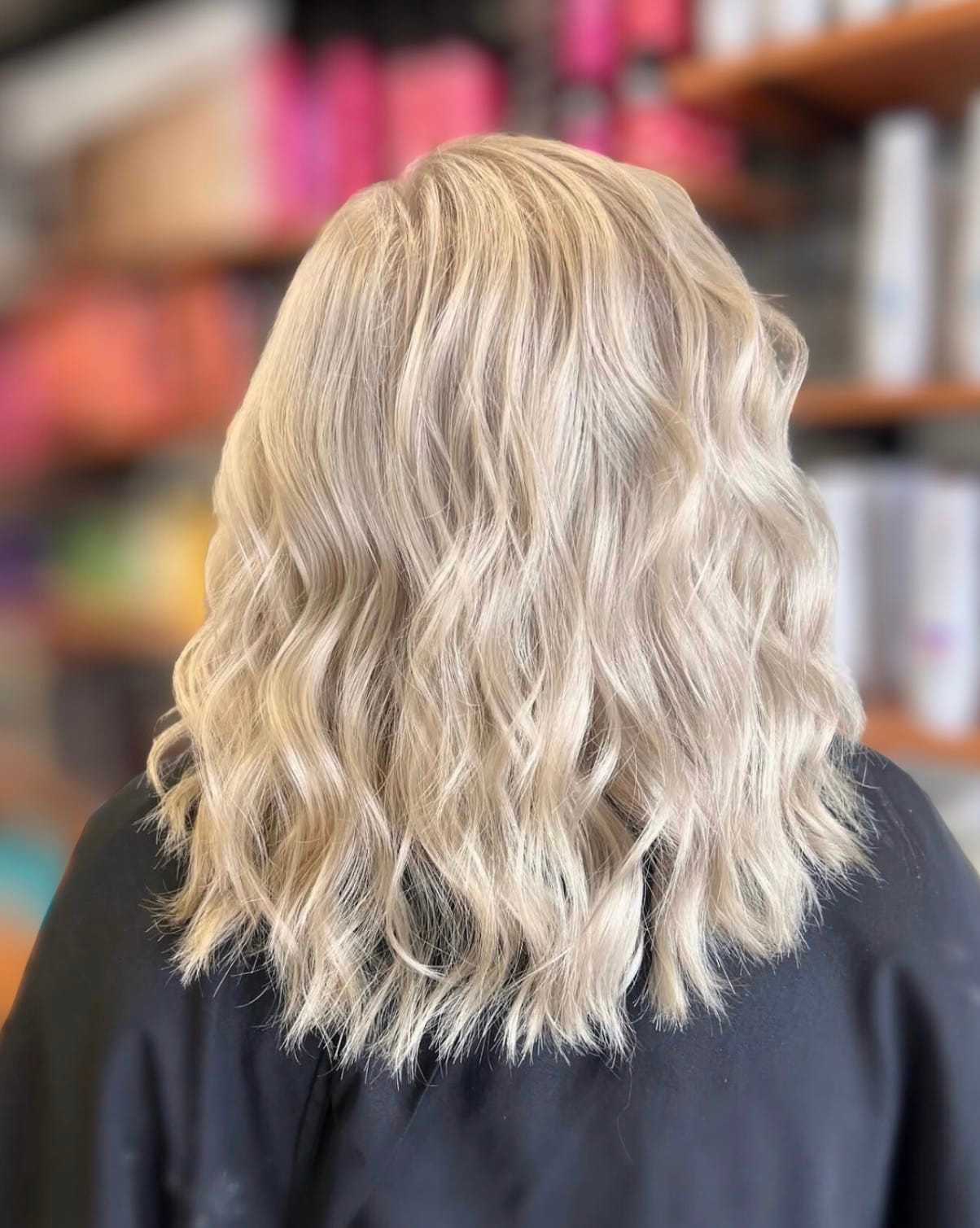 Wavy blonde hairstyle with soft curls viewed from the back in a salon setting.