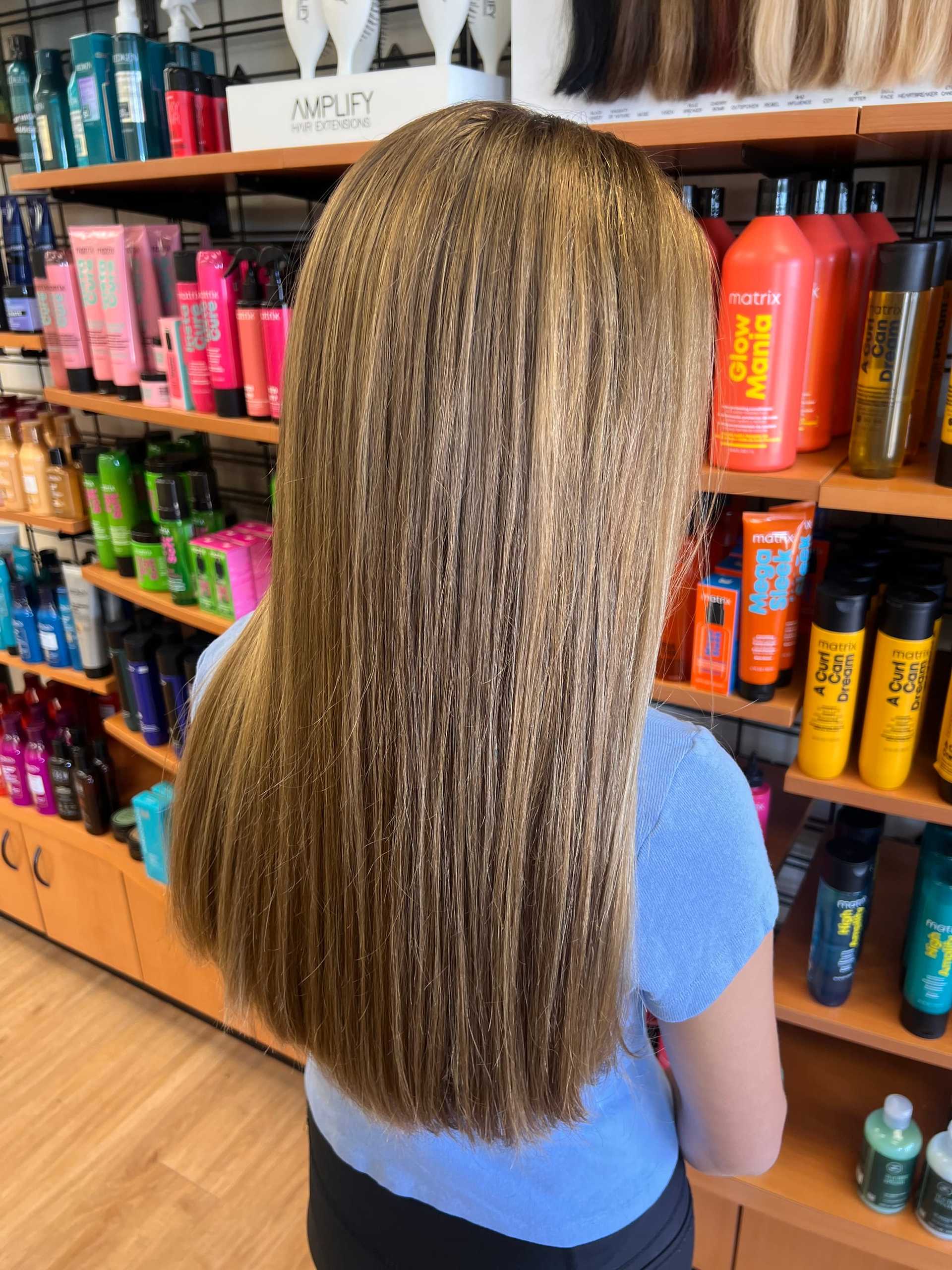 Straight, highlighted hair against a backdrop of colorful hair care products on shelves.