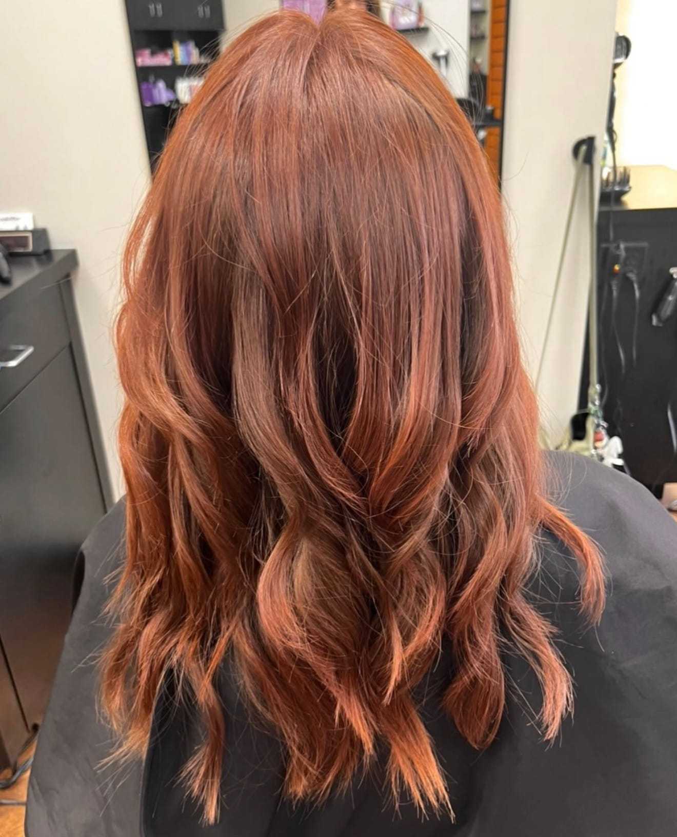 Wavy auburn hair styled in a salon setting, viewed from the back.