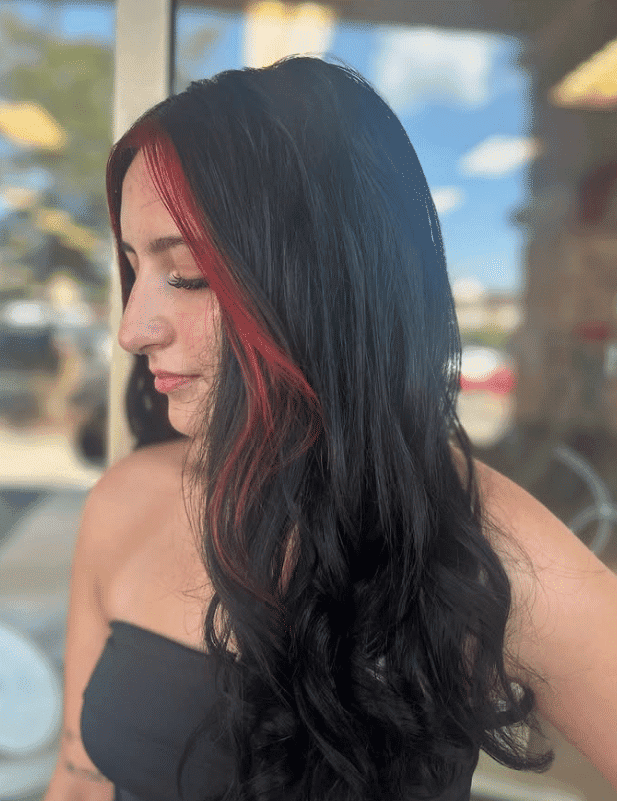 Woman with long, wavy black hair and striking red highlights standing outside in daylight.