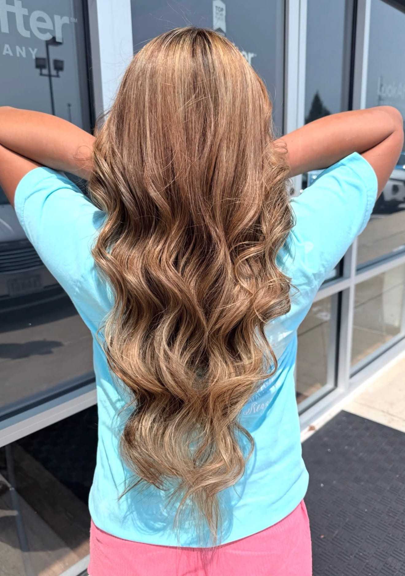 Long, wavy hair cascading down the back of a person standing outside a building.
