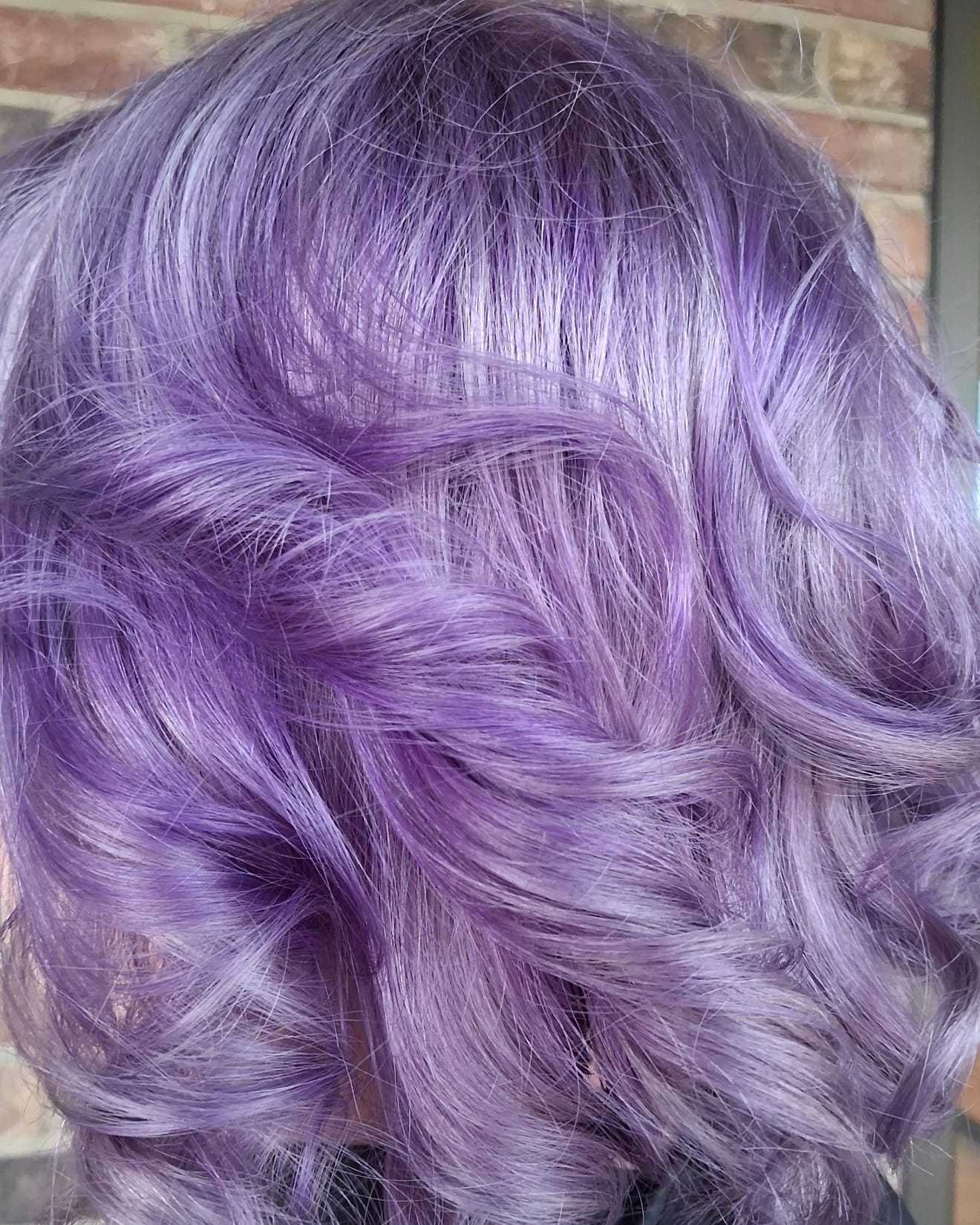 Purple wavy hair with soft curls against a brick wall background.