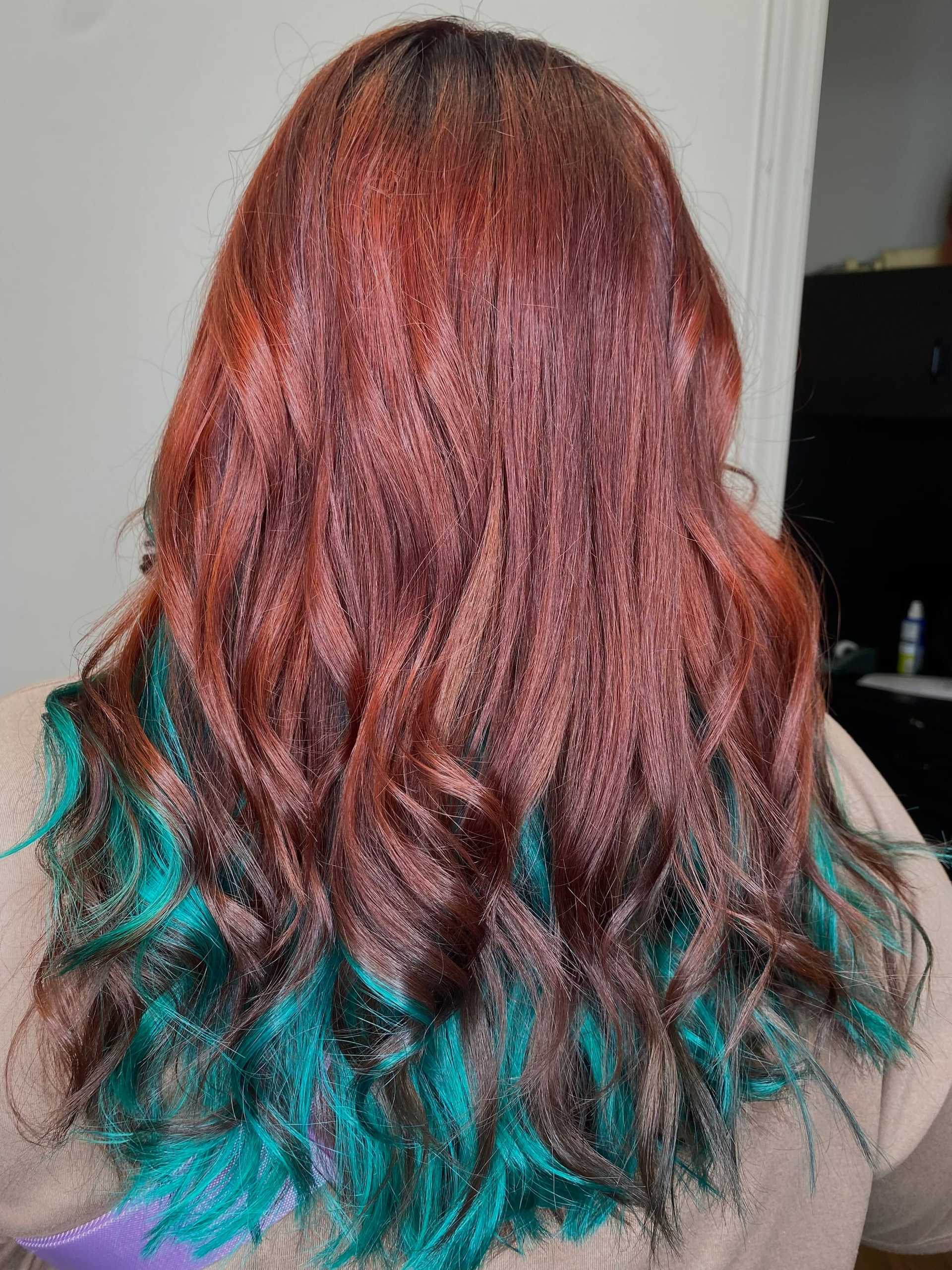 Red hair with turquoise ombre, styled in loose waves against a neutral background.
