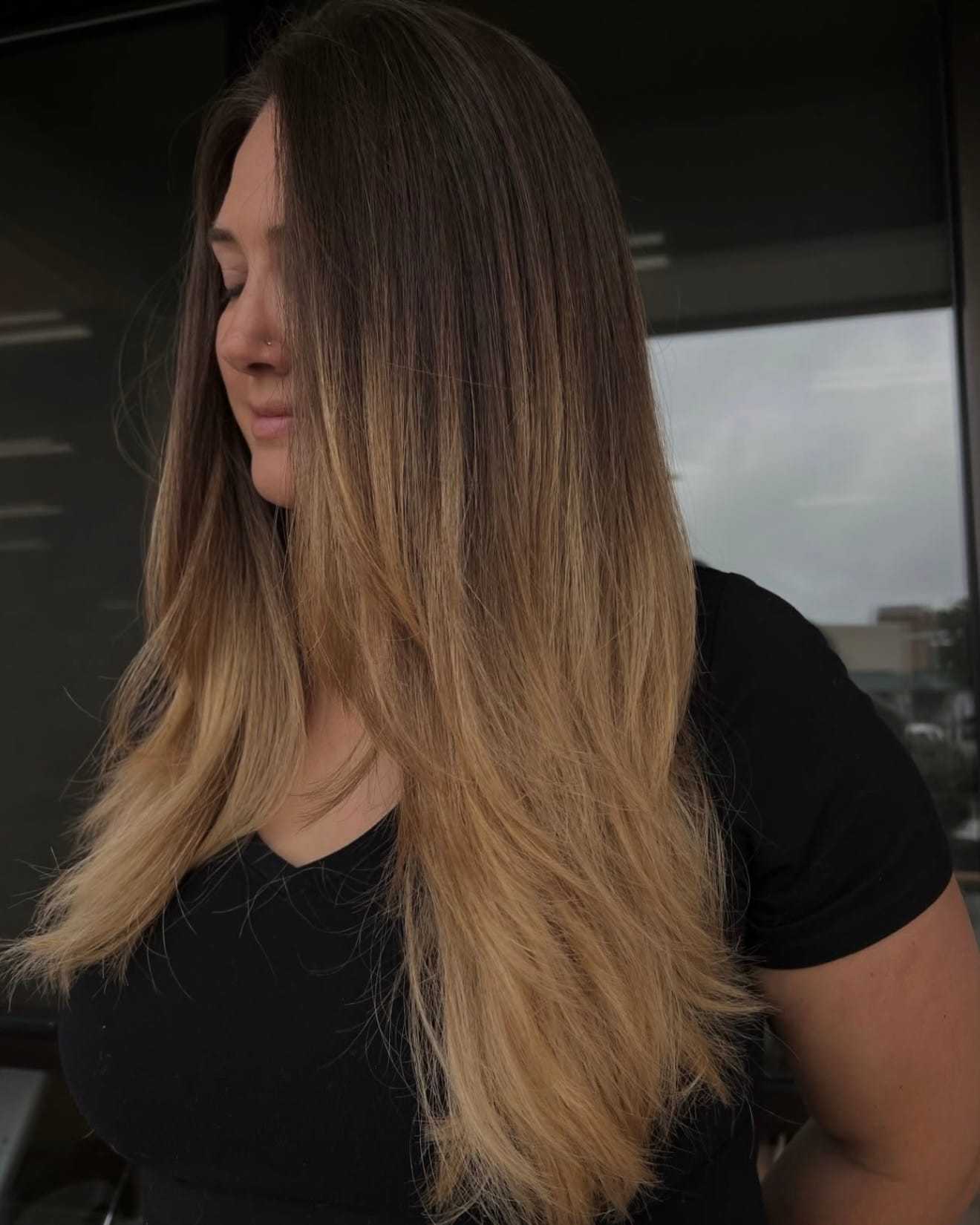 Young woman with long, flowing ombre hair stands outside wearing a black top.