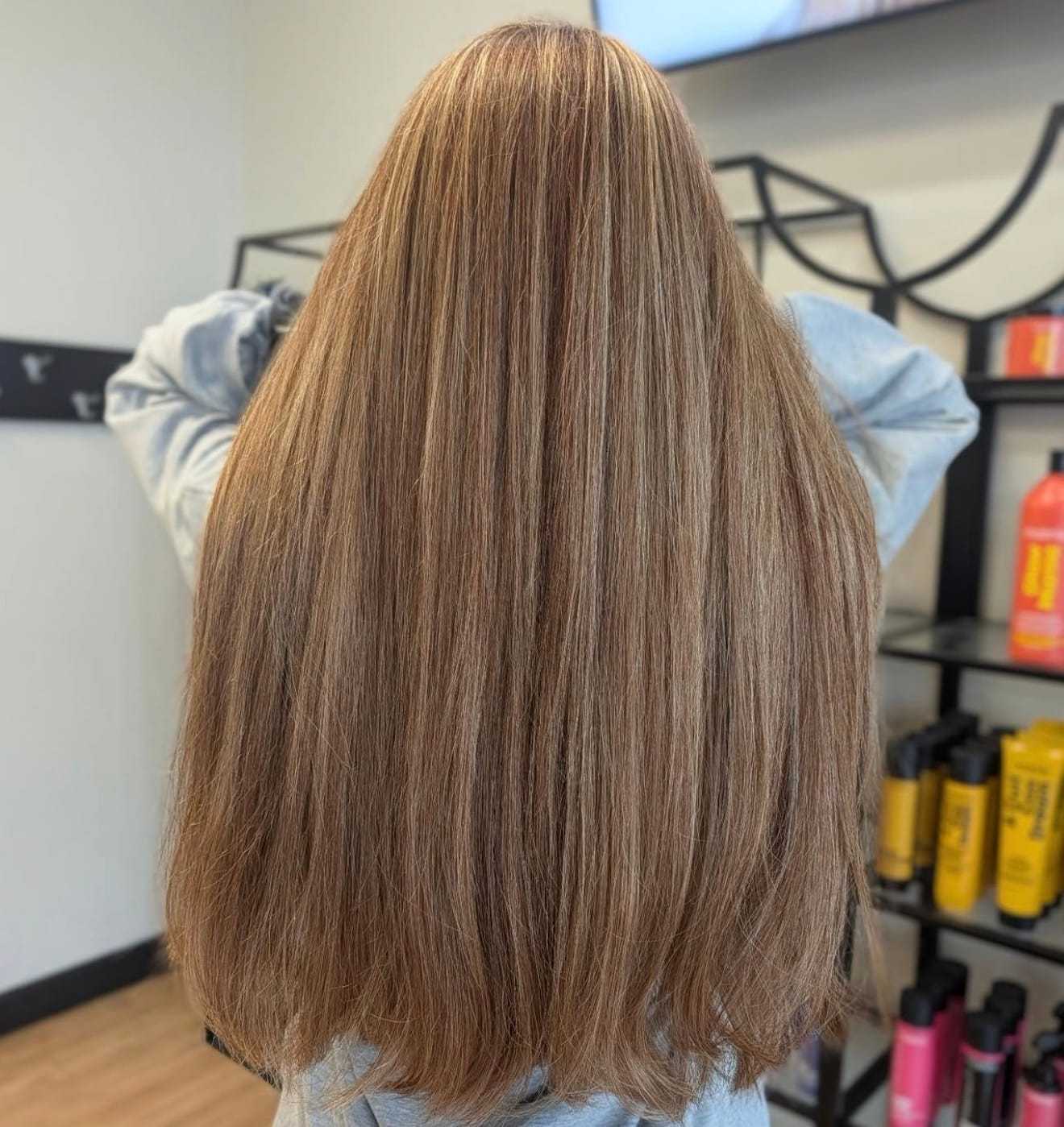 Long, straight brown hair with highlights, styled indoors near salon products.