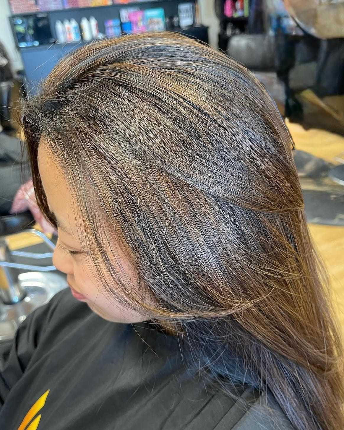 Woman with highlighted brown hair getting styled at a salon, wearing a black cape.