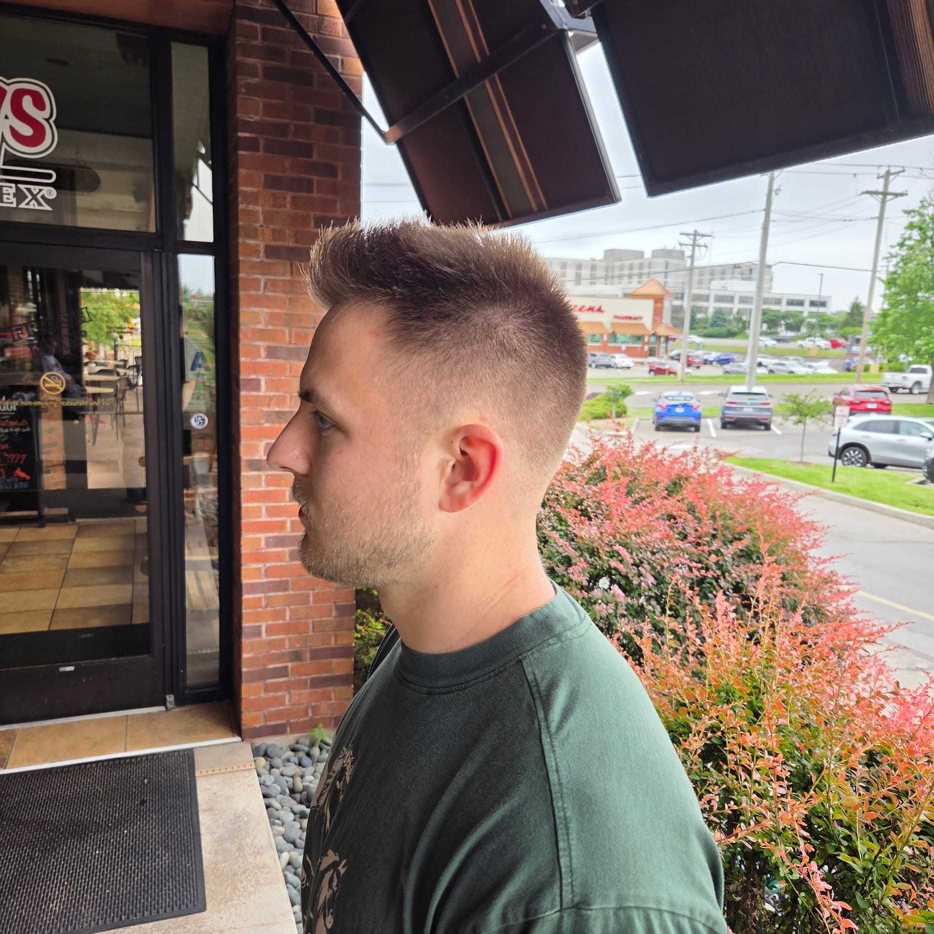 Man with a fresh haircut standing outside a barbershop, looking at a parking lot.