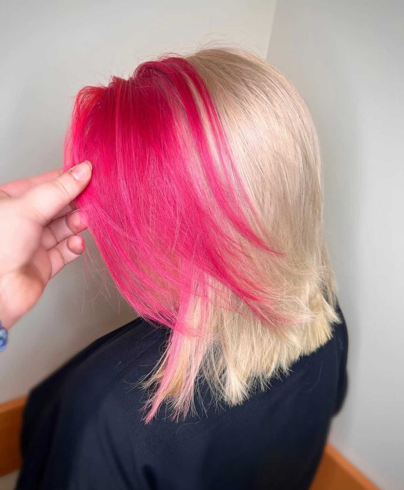 Blonde hair with vibrant pink highlights being styled in a salon.