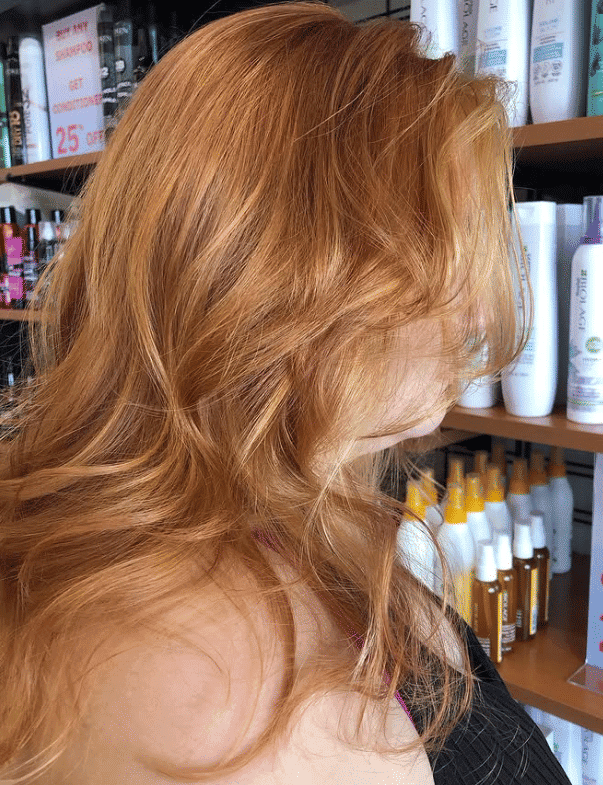 Shoulder-length wavy auburn hair, salon products in the background.