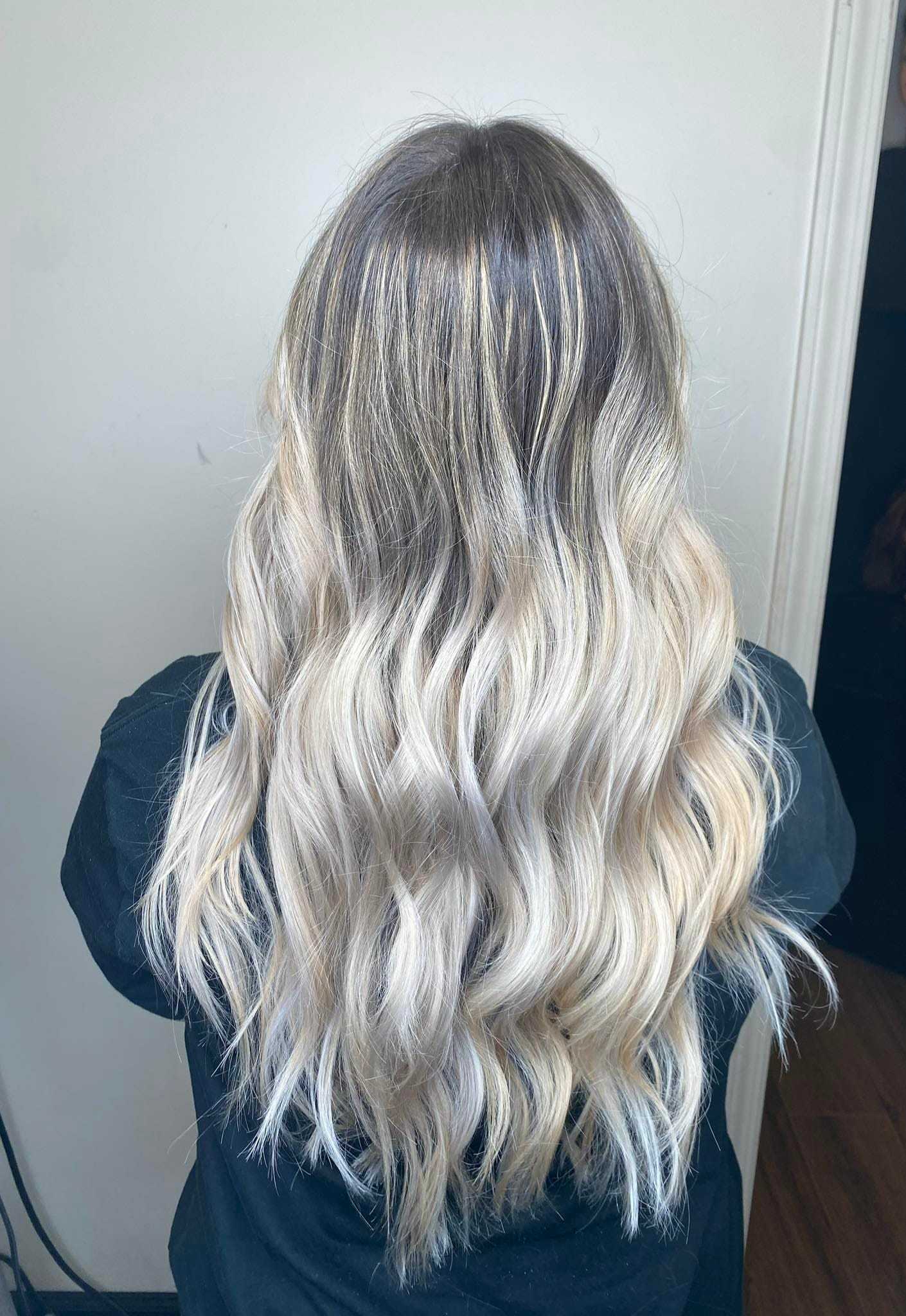 Blonde hair with dark roots, styled in soft waves, viewed from the back.