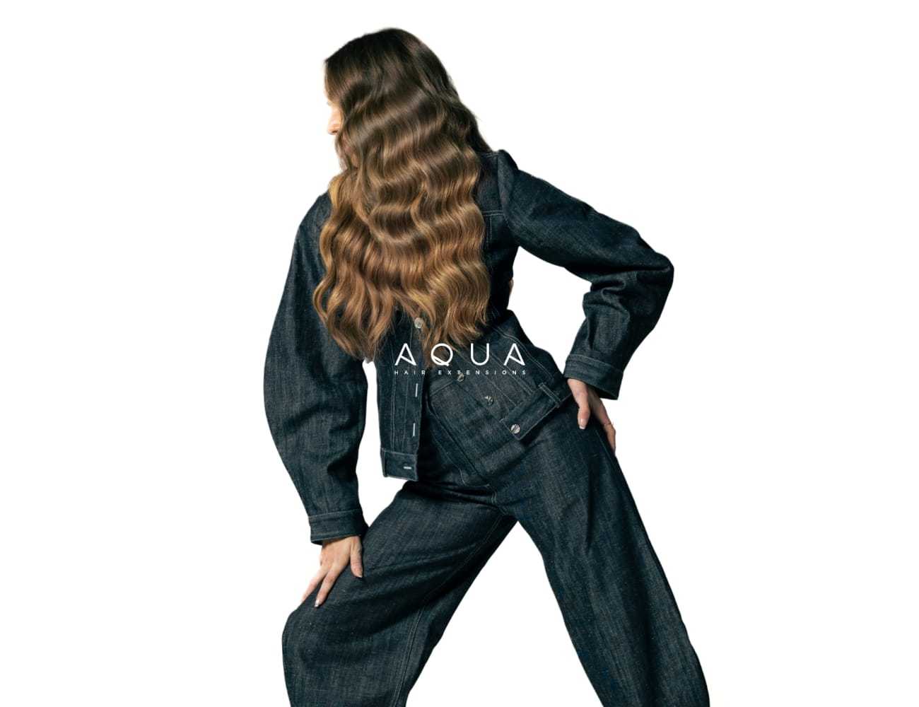 A person wearing a denim outfit with long, wavy hair, posing stylishly.