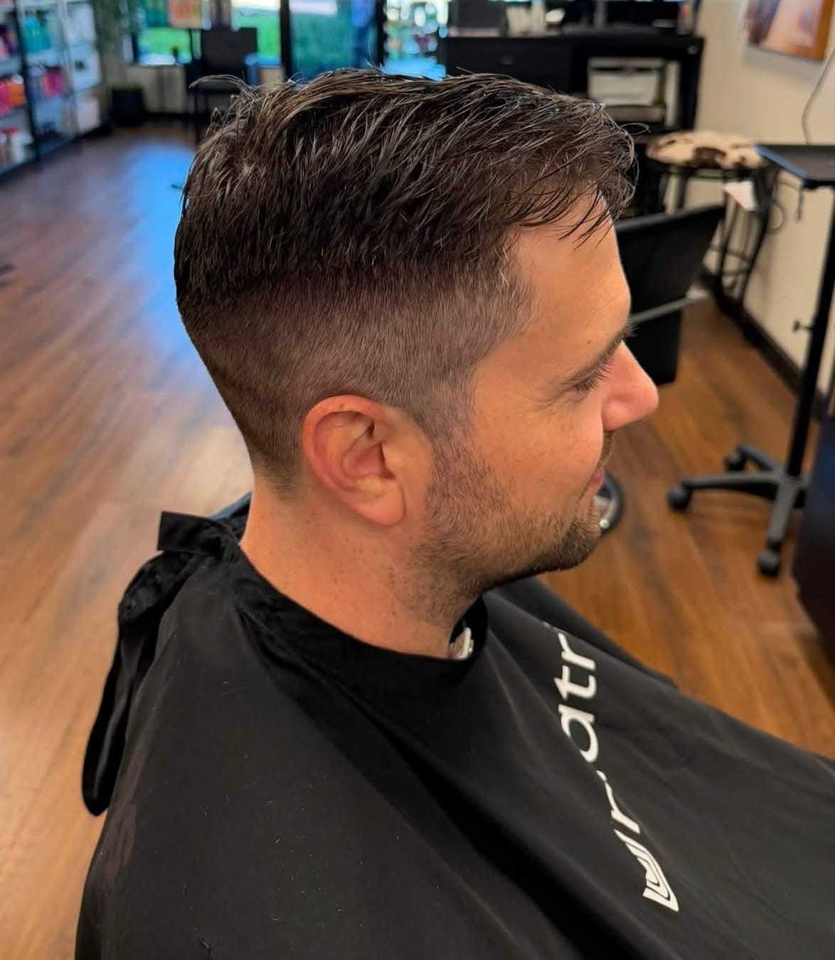 Man with short haircut at a barbershop, sitting in a black cape.