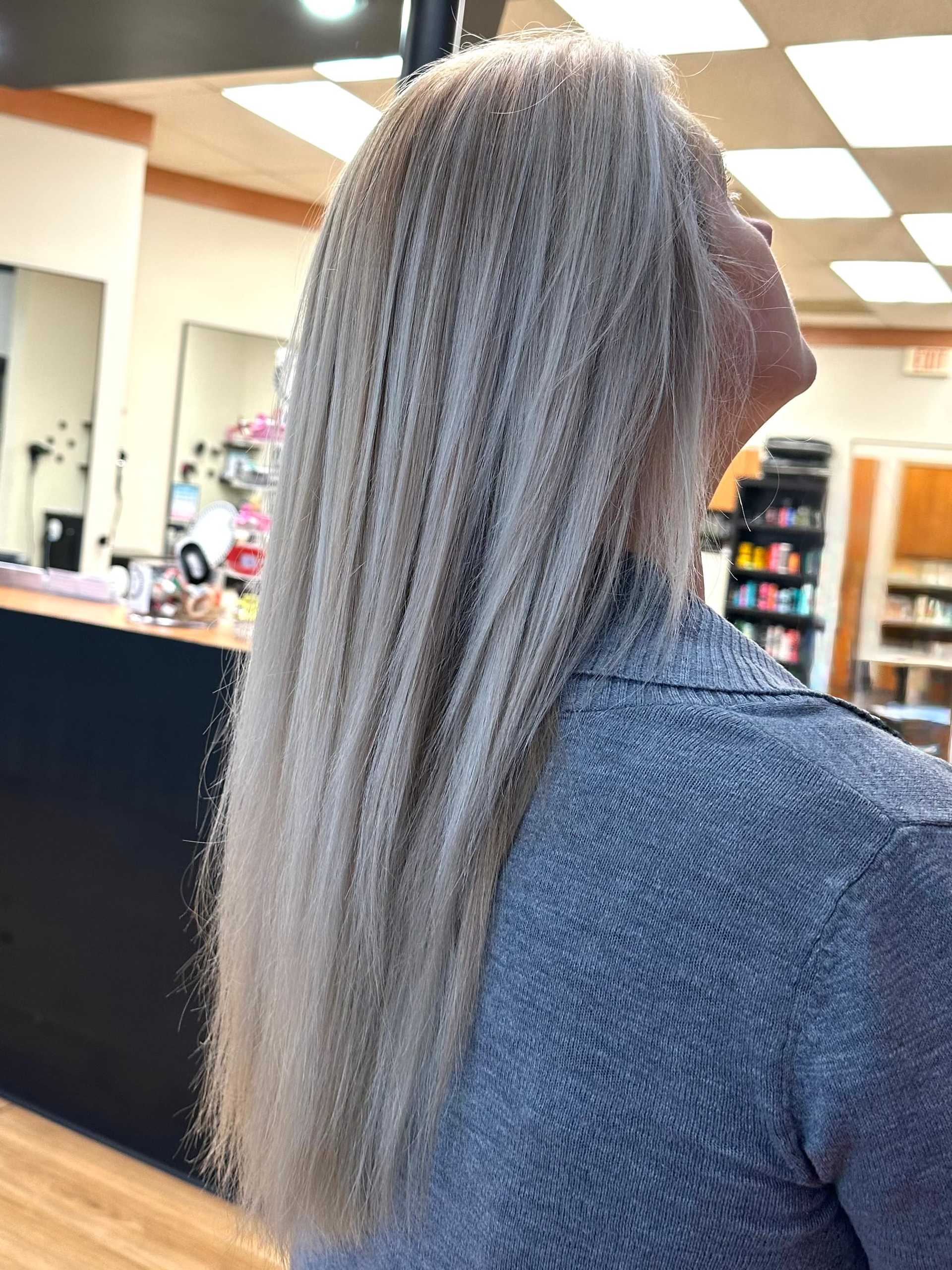 Blonde woman shows off long, straight hair in a salon setting.