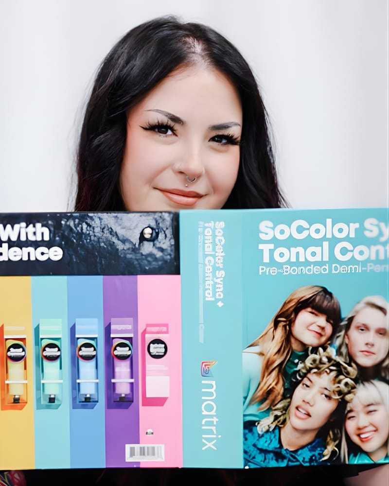 Woman holding a colorful Matrix hair color product brochure, smiling at the camera.