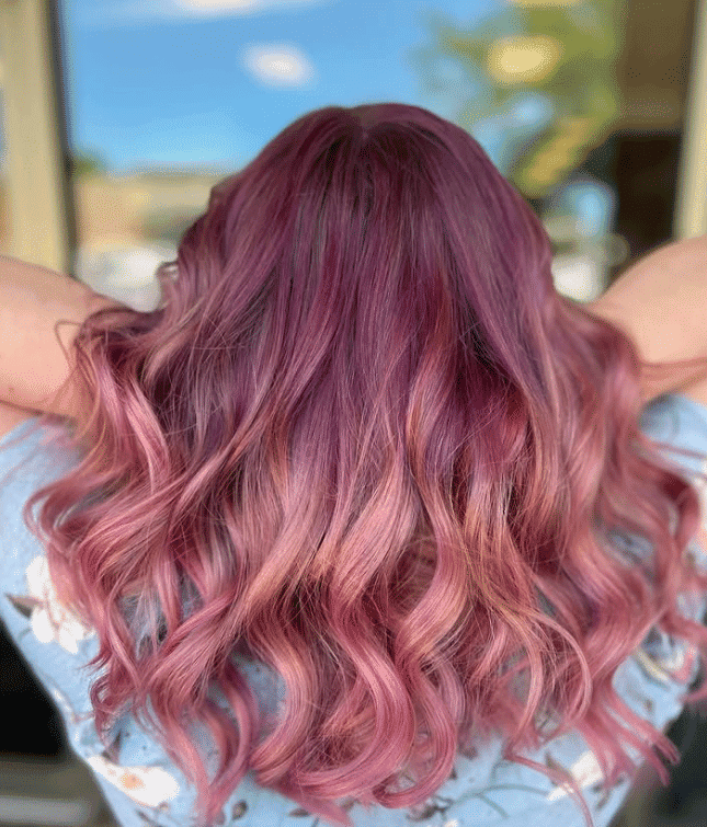 Wavy hair dyed in vibrant shades of pink and purple against a blurred background.