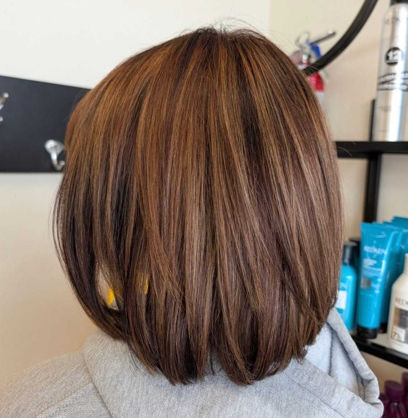 Short brown bob haircut with subtle highlights, displayed in a salon setting.