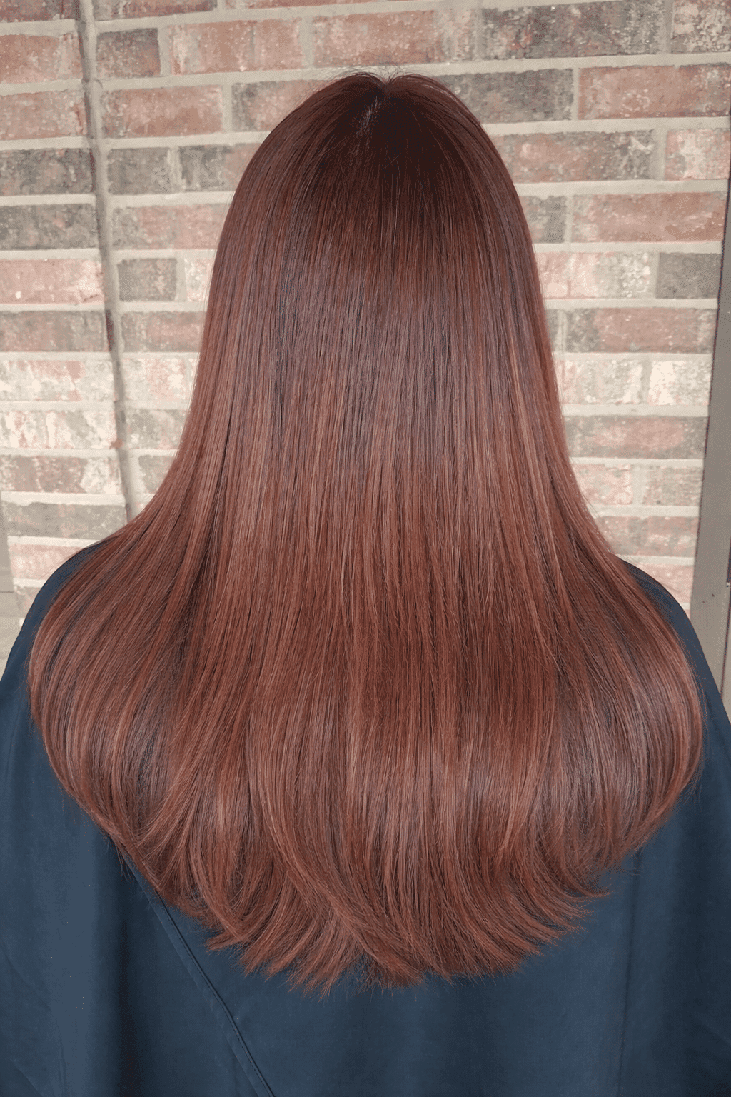 Long, straight auburn hair against a brick wall background.