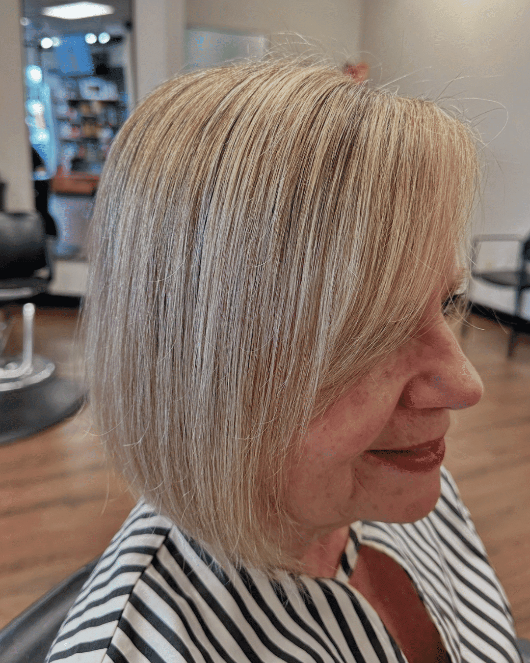 Short blonde bob haircut in a salon setting, woman smiling in profile.