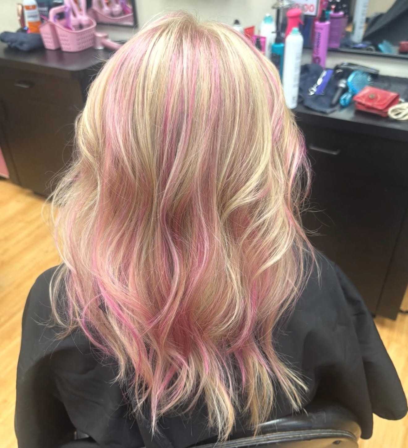 Blonde hair with pink highlights styled in loose waves in a salon setting.